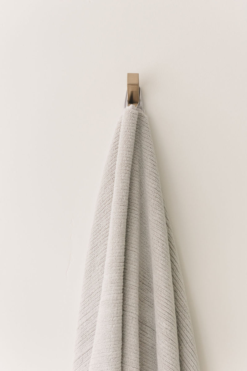 Ribbed Terry Bath Towel in the color Light Grey. Photo of Ribbed Terry Bath Towel taken as the Light Grey Ribbed Terry Bath Towel is hanging from a towel hook in a bathroom.