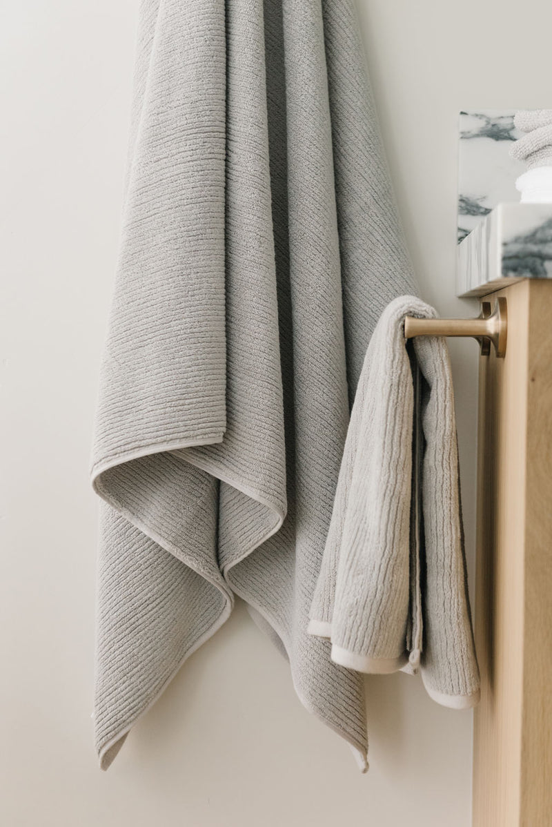 Ribbed Terry Bath Towel and Hand Towel in the color Light Grey. Photo of Ribbed Terry Bath Towel and Hand Towel taken as the Light Grey Ribbed Terry Bath Towel and Hand Towel is hanging from a towel hook in a bathroom.