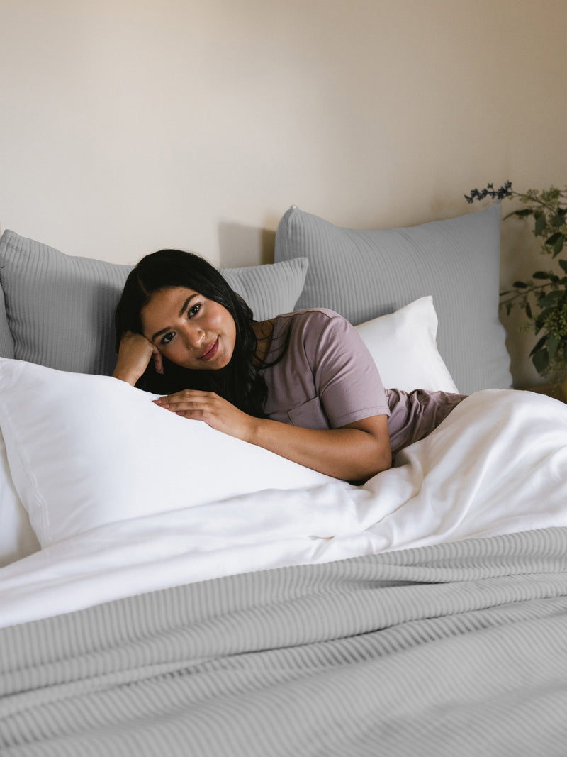 Woman laying in a bed with light grey coverlet and shams