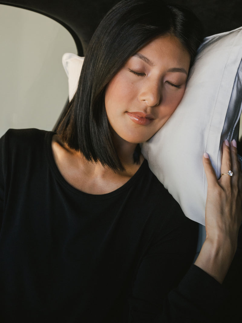 Woman laying on light grey travel pillow in the car