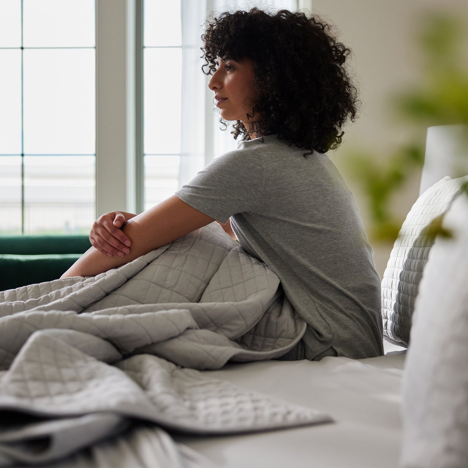 Woman sitting in bed with light grey bamboo jersey sheets and quilt 