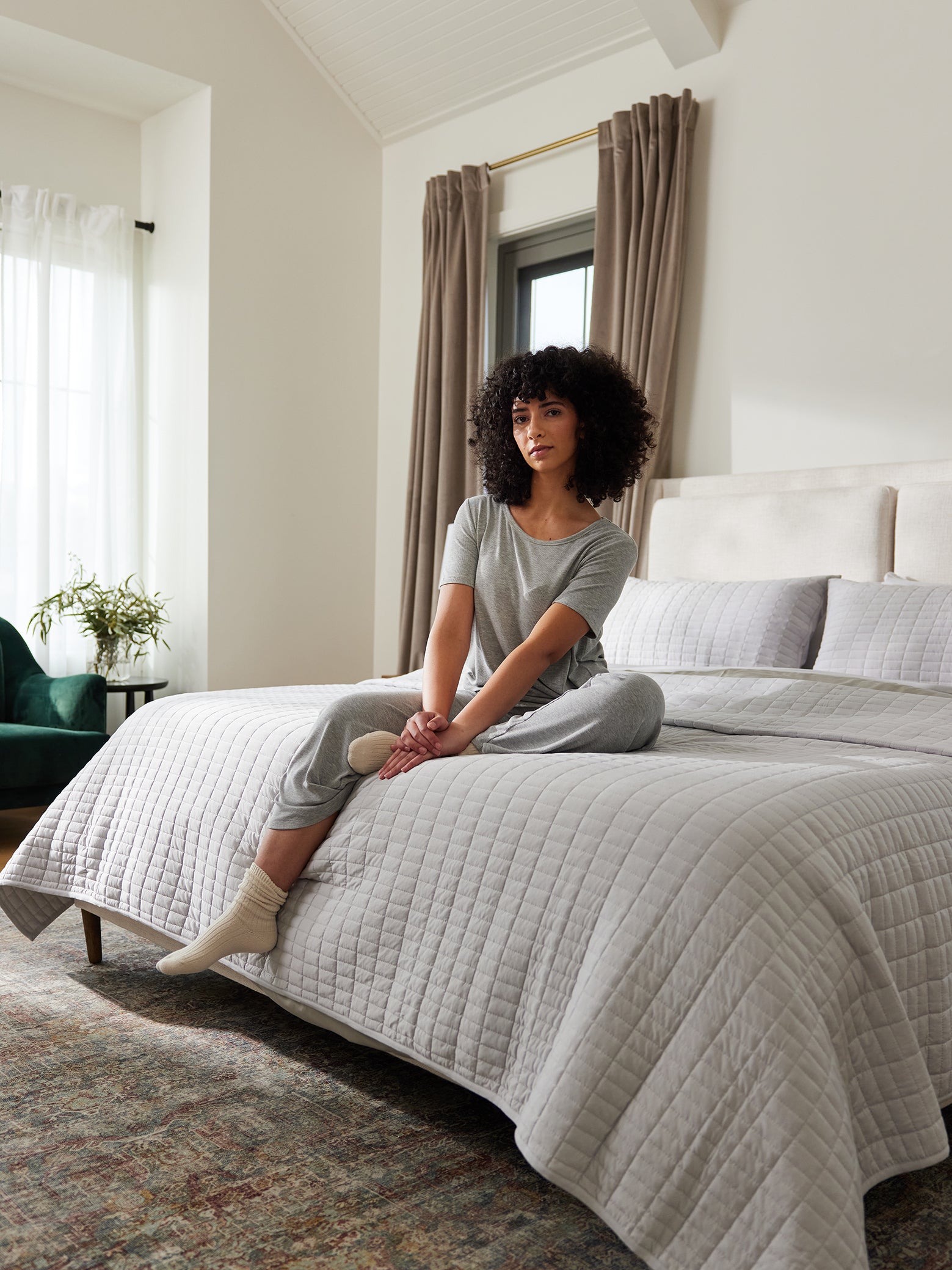Woman sitting on bed made with light grey bamboo jersey bedding and quilt 