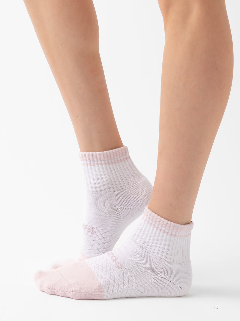 Close-up of a person's legs wearing Cozy Earth's Essential Quarter Sock 2-Pack in white with light pink toes and heels. The background is plain and white, emphasizing the socks and lower legs.