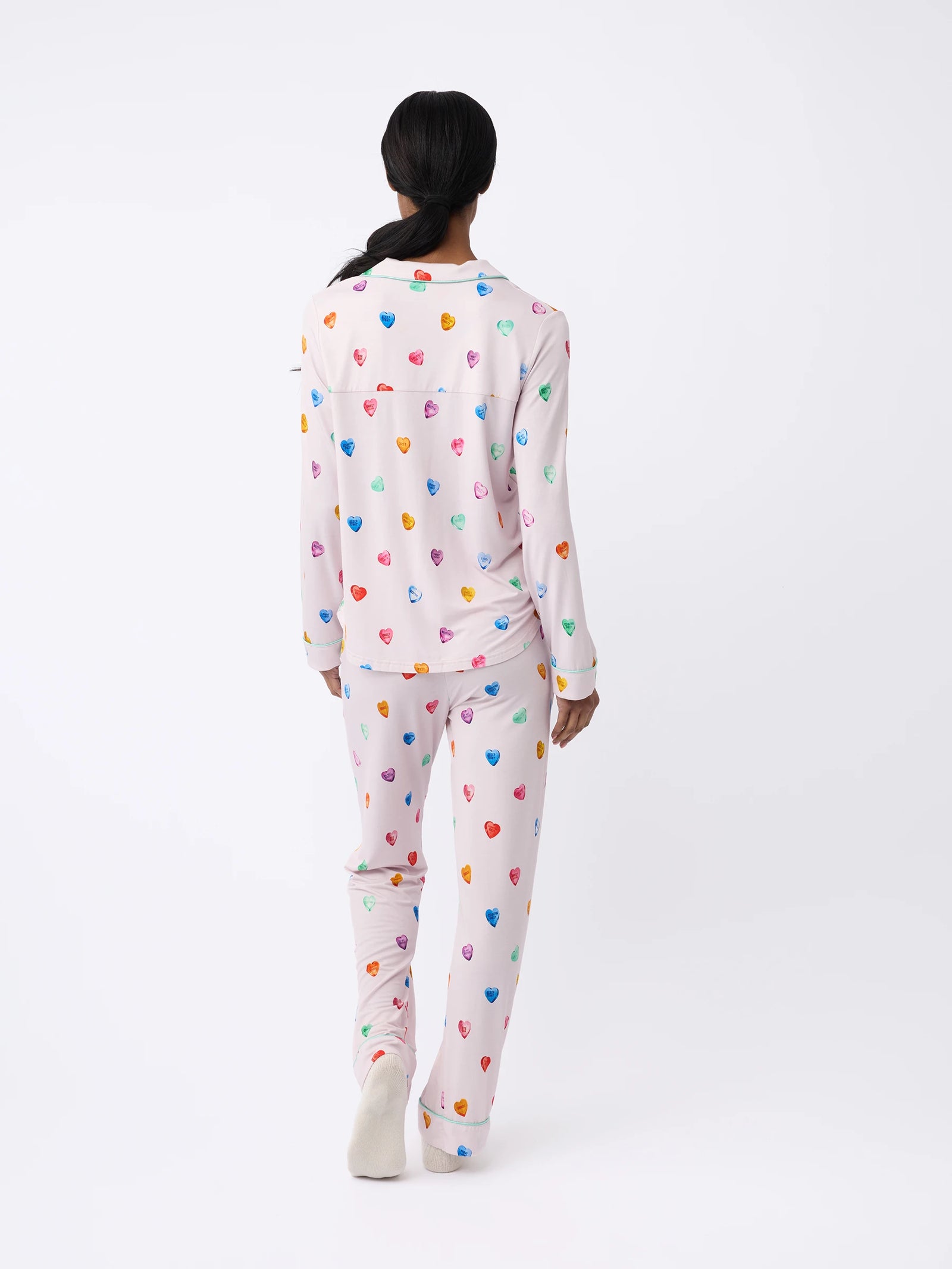 A person is wearing the Women's Stretch-Knit Bamboo Pajama Pant by Cozy Earth, featuring a colorful heart pattern. They are standing with their back to the camera against a plain white background. 