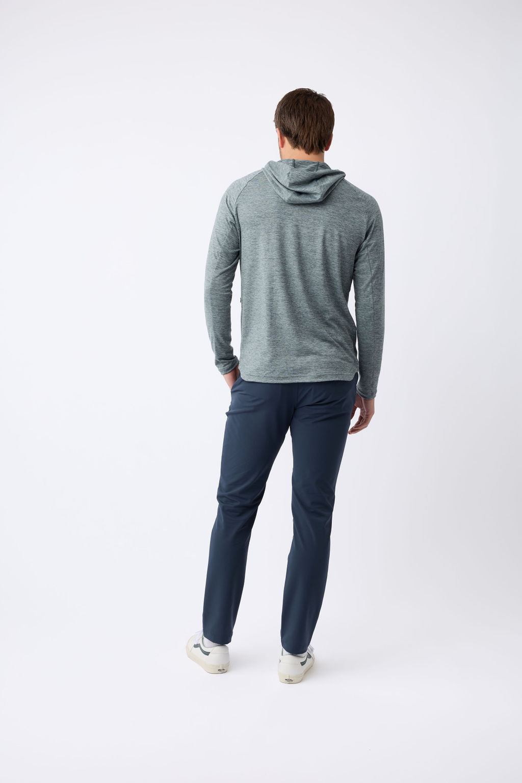 A man wearing a Cozy Earth Men's Lightweight Performance Hoodie in gray paired with dark blue pants and white sneakers stands against a plain white background, facing away. |Color:Heather Dawn