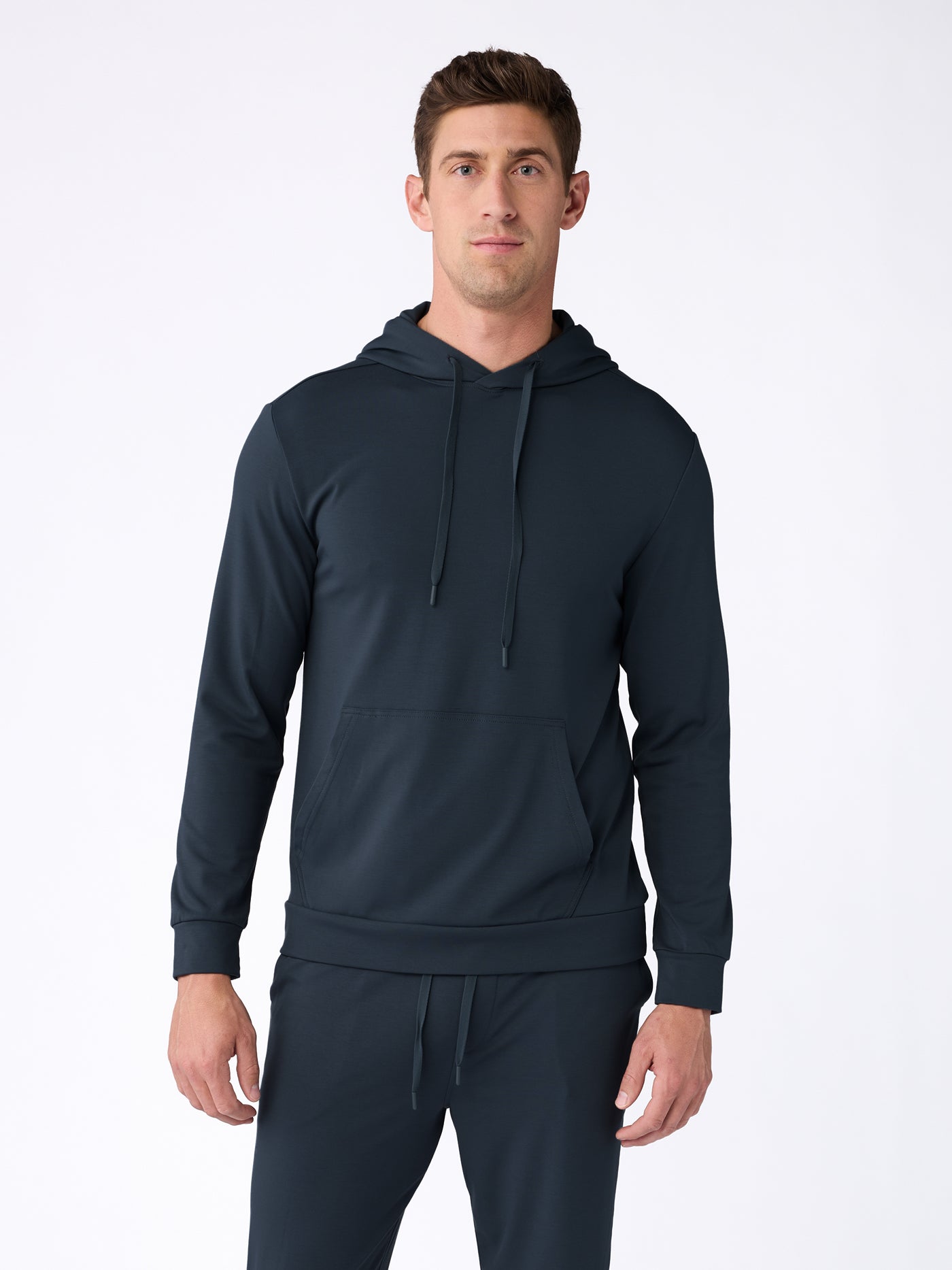 A man wears the Cozy Earth Men's Brushed Bamboo Hoodie & Jogger Set in dark navy, featuring a hooded sweatshirt with front pockets and matching jogger pants, standing facing forward against a plain white background. |Color:Navy