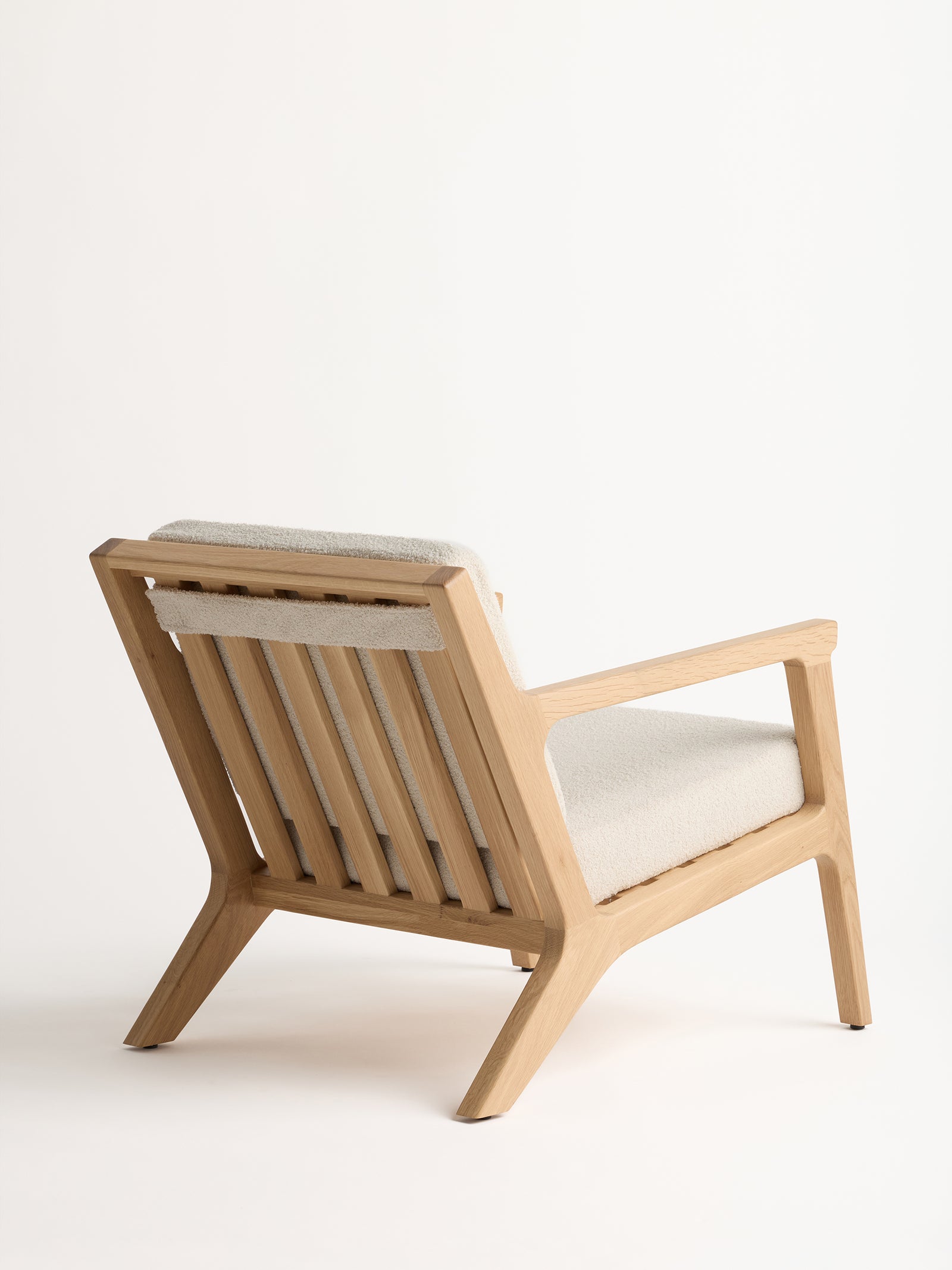 The Coronado Lounge Chair by Cozy Earth is displayed from both the back and side, set against a plain white background. This wooden armchair includes a light beige cushion and showcases a sleek, minimalist design with straight lines and a natural wood finish. 