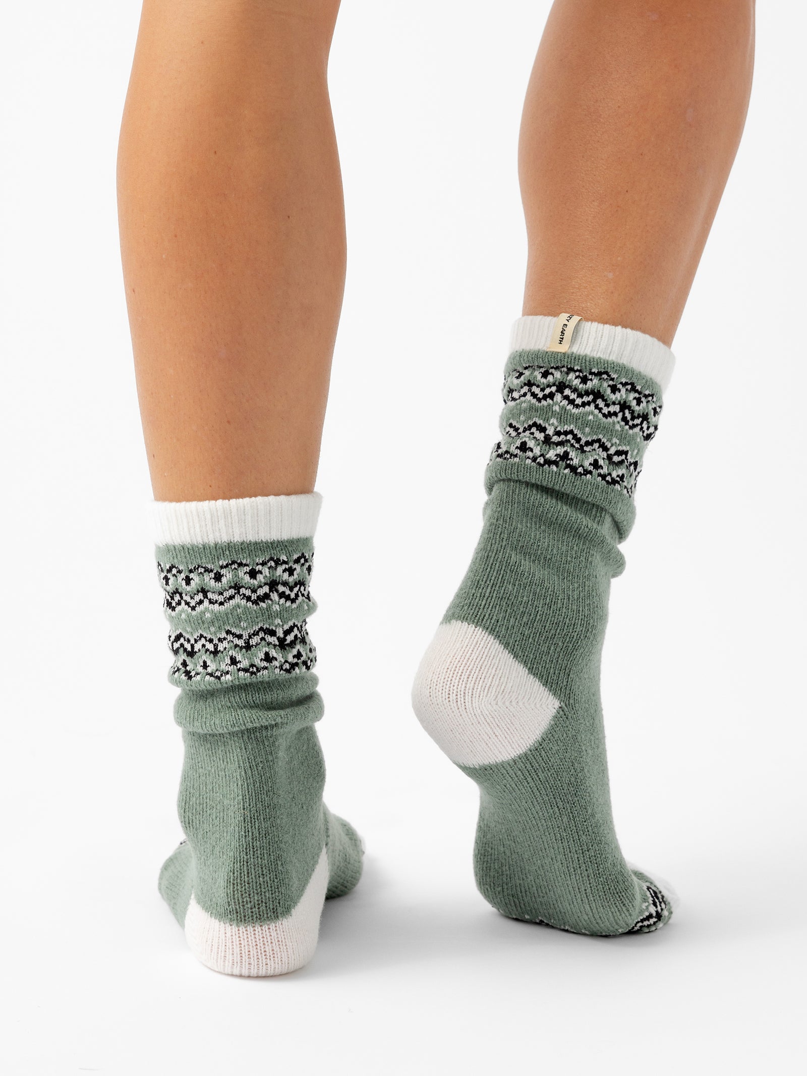 A person stands facing backwards in front of a white background wearing Fair Isle Plush Lounge Socks in Oakmoss. 