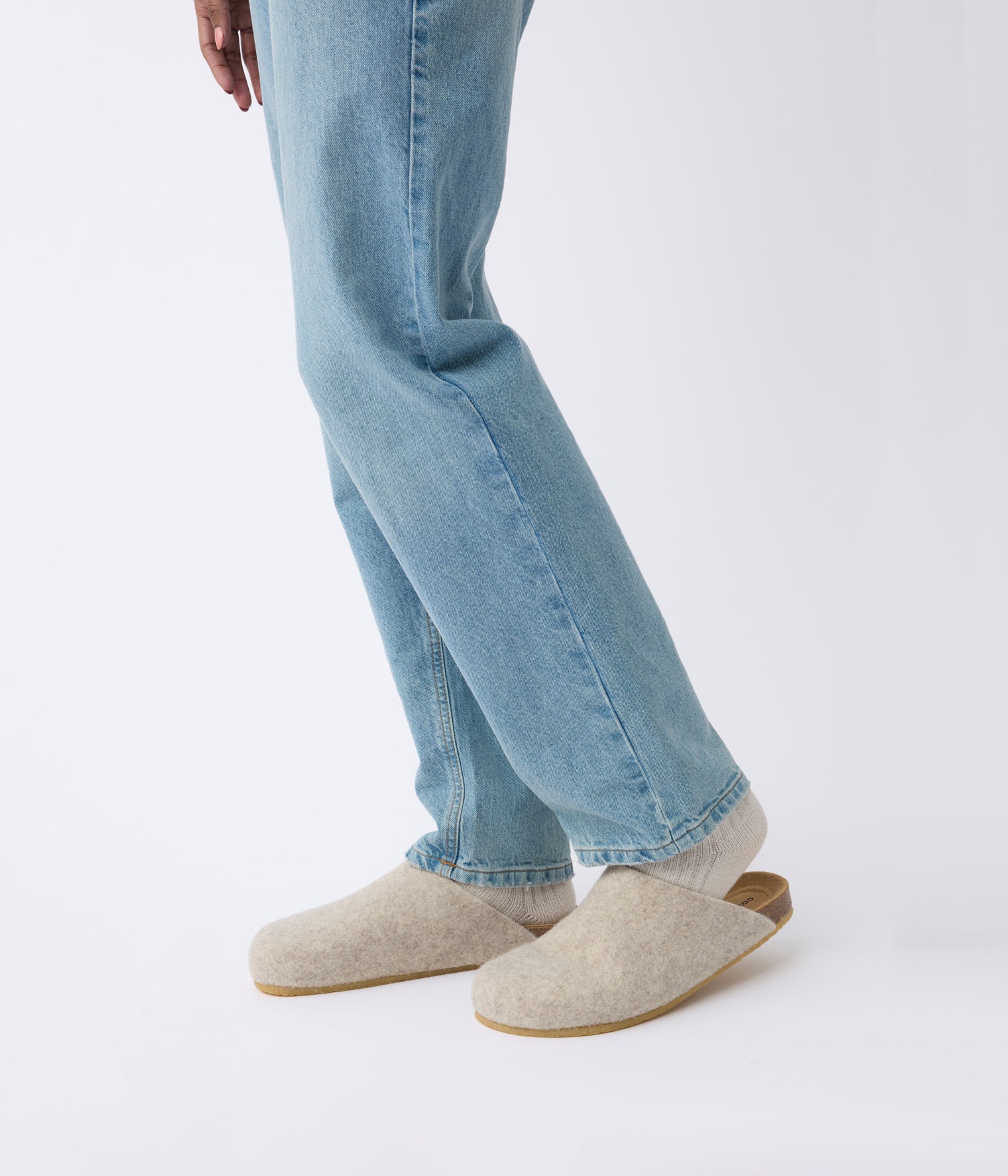 A person wearing light blue jeans and the Cozy Earth Lakehouse Clog with cream-colored socks stands against a plain white background, showing only the lower half of their body. 