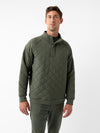 A person stands against a plain white background, donning the Men's Ultra-Soft Bamboo Quilted Snap Pullover from Cozy Earth. The green pullover features a high collar and snap-button closure. The individual, with short light brown hair, looks directly at the camera with a relaxed and confident posture. |Color:Olive