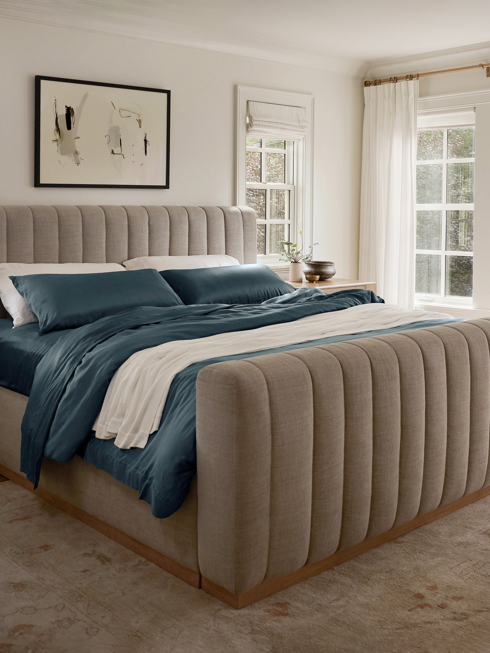 Zoomed out image of bed with pacific blue bedding and a blanket draped over it 