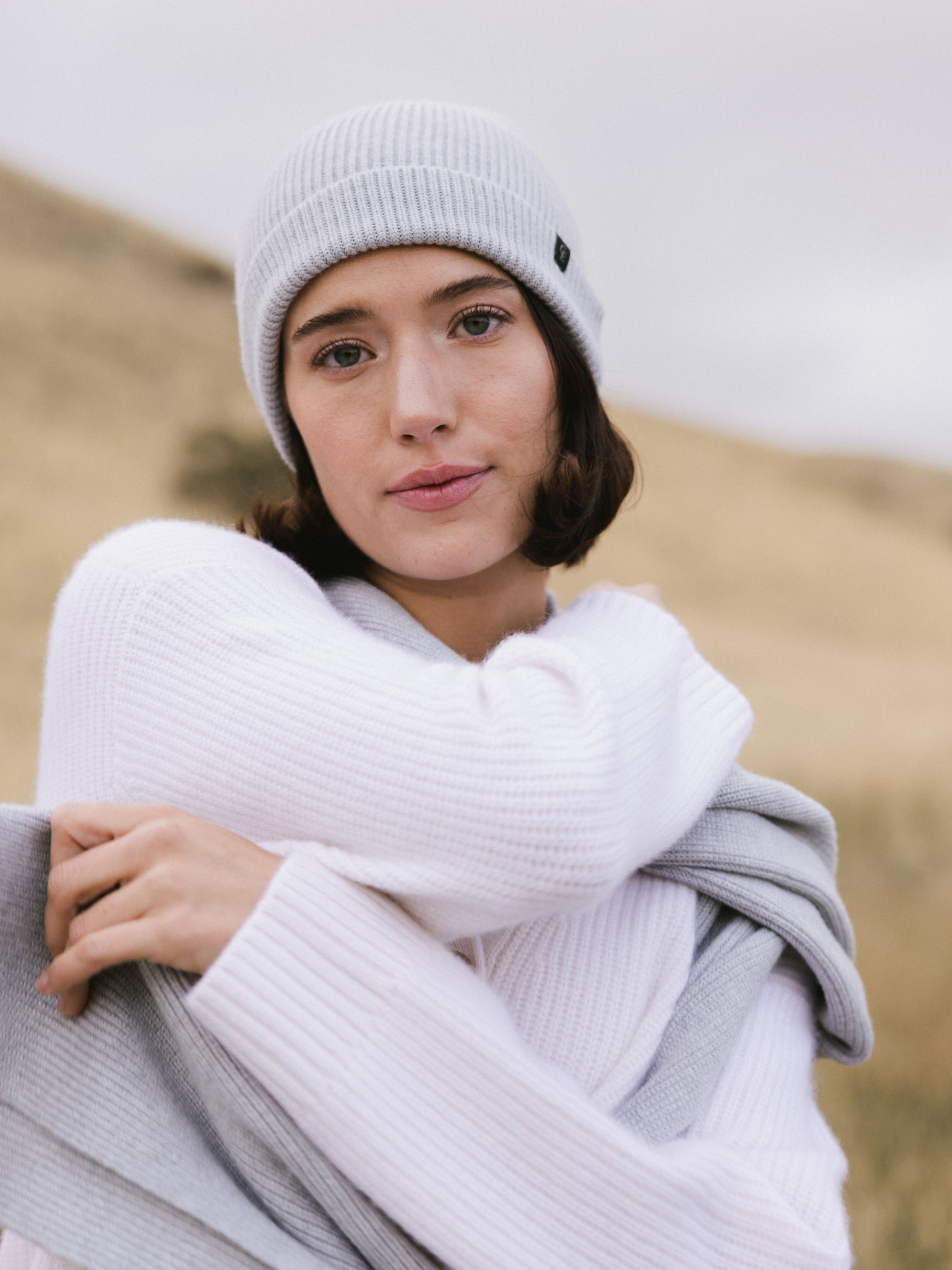 Woman wearing a light gray knit beanie and scarf in a field 