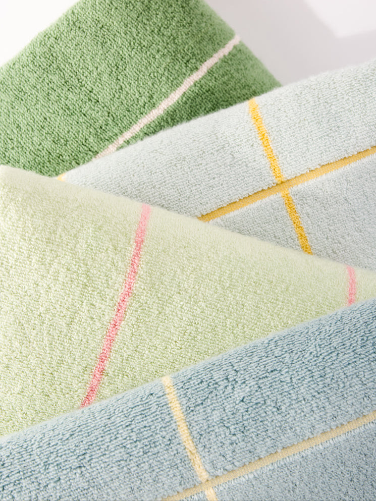 Three Windowpane Resort Towels by Cozy Earth, in pastel green, light blue, and mint, are stacked diagonally. Each towel displays a subtle plaid pattern featuring thin lines in pink, yellow, and blue on a plain white background. |Color:Prickly Pear