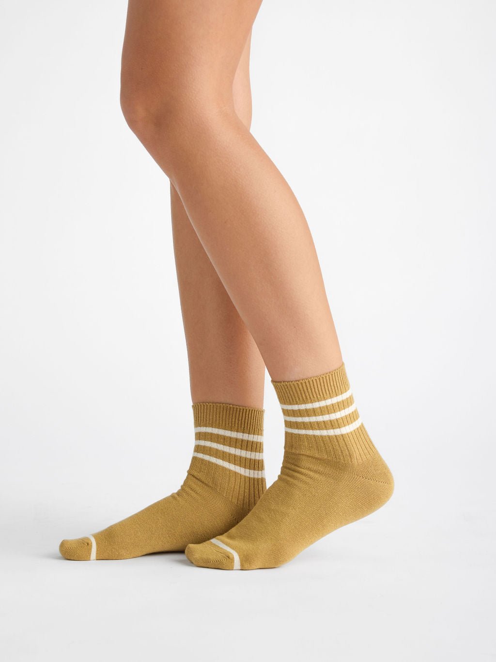 A person wears Cozy Earth's Women's Sadie Sock in mustard yellow with white stripes, standing on a white background. The mid-calf socks feature feet positioned with one slightly ahead of the other. 