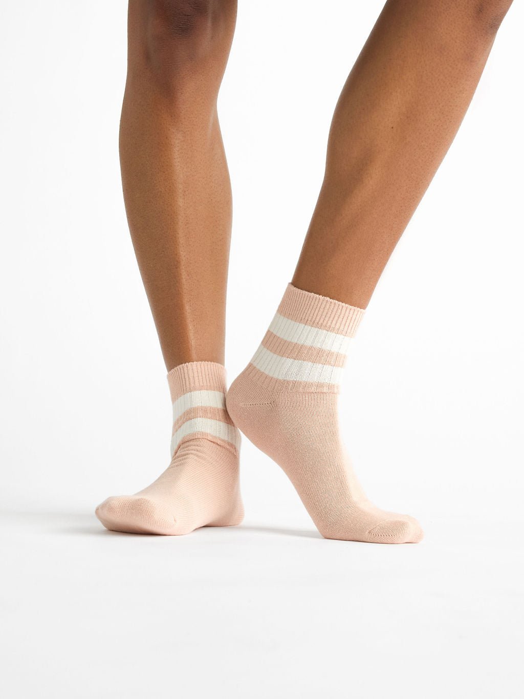 A person models the Women's Sadie Sock by Cozy Earth, featuring a peach shade with two white stripes, standing slightly foot forward against a plain white backdrop. |Color:Dusty Rose/Bone