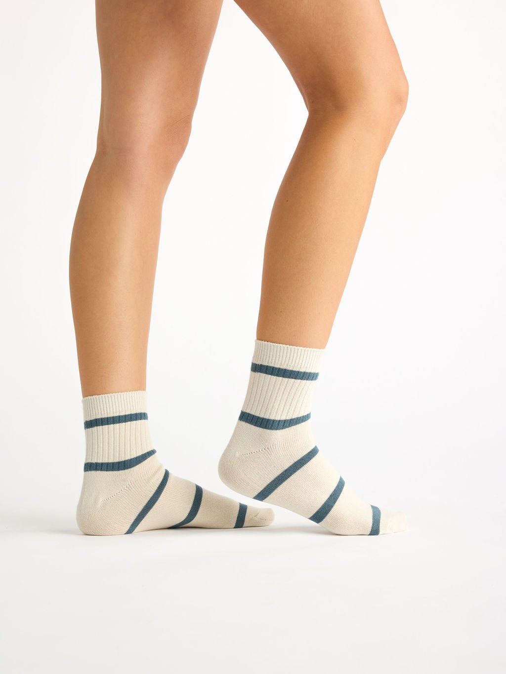 A person is wearing Cozy Earth's Women's Sadie Sock, featuring cream-colored fabric with dark blue stripes, against a plain background. The focus is on their lower legs and feet. 