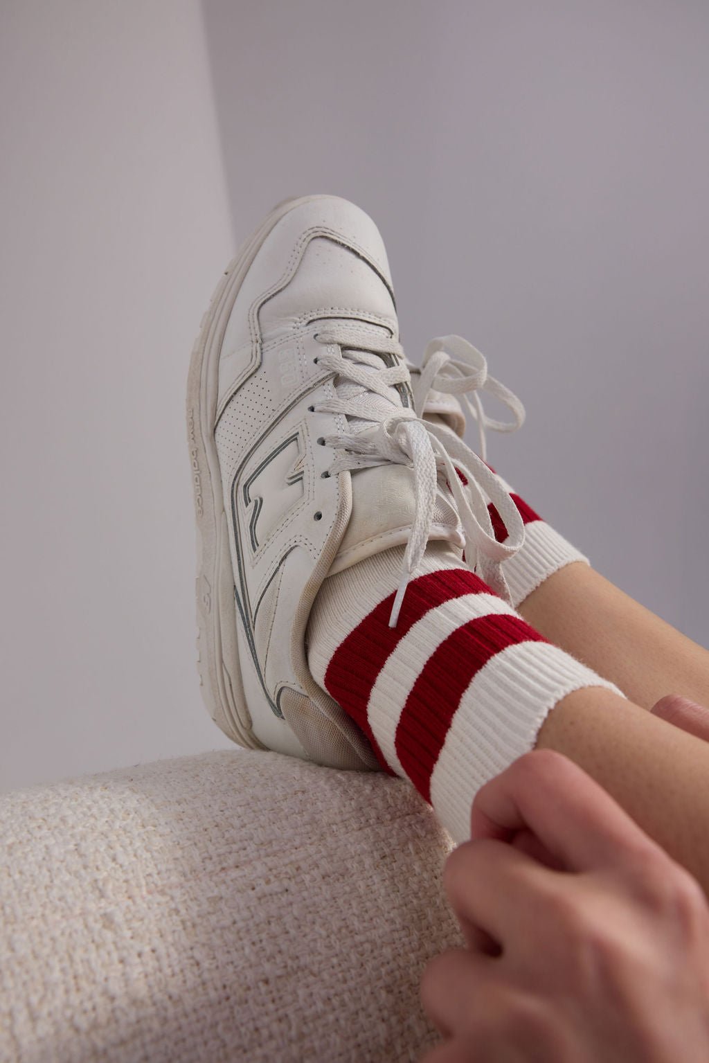 A person wearing Cozy Earth's Women's Sadie Sock, featuring a white design with two red stripes wears white tennis shoes. 