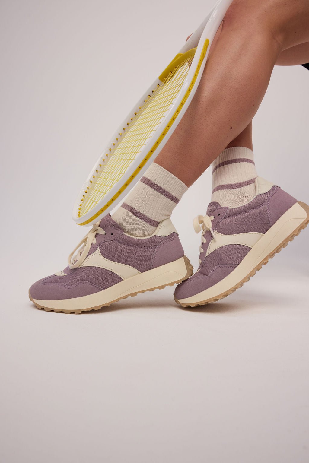 A person wearing Cozy Earth's Women's Sadie Sock, featuring cream color with purple stripes, is standing on a light gray surface. Only the lower legs and feet are visible. |Color:Parchment/Dusty Orchid