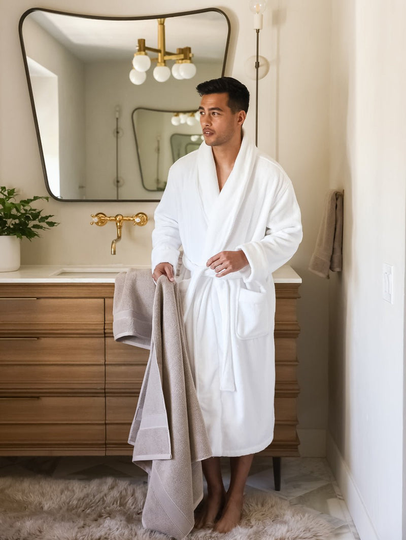 Man in white robe standing in bathroom with sand luxe bath sheet