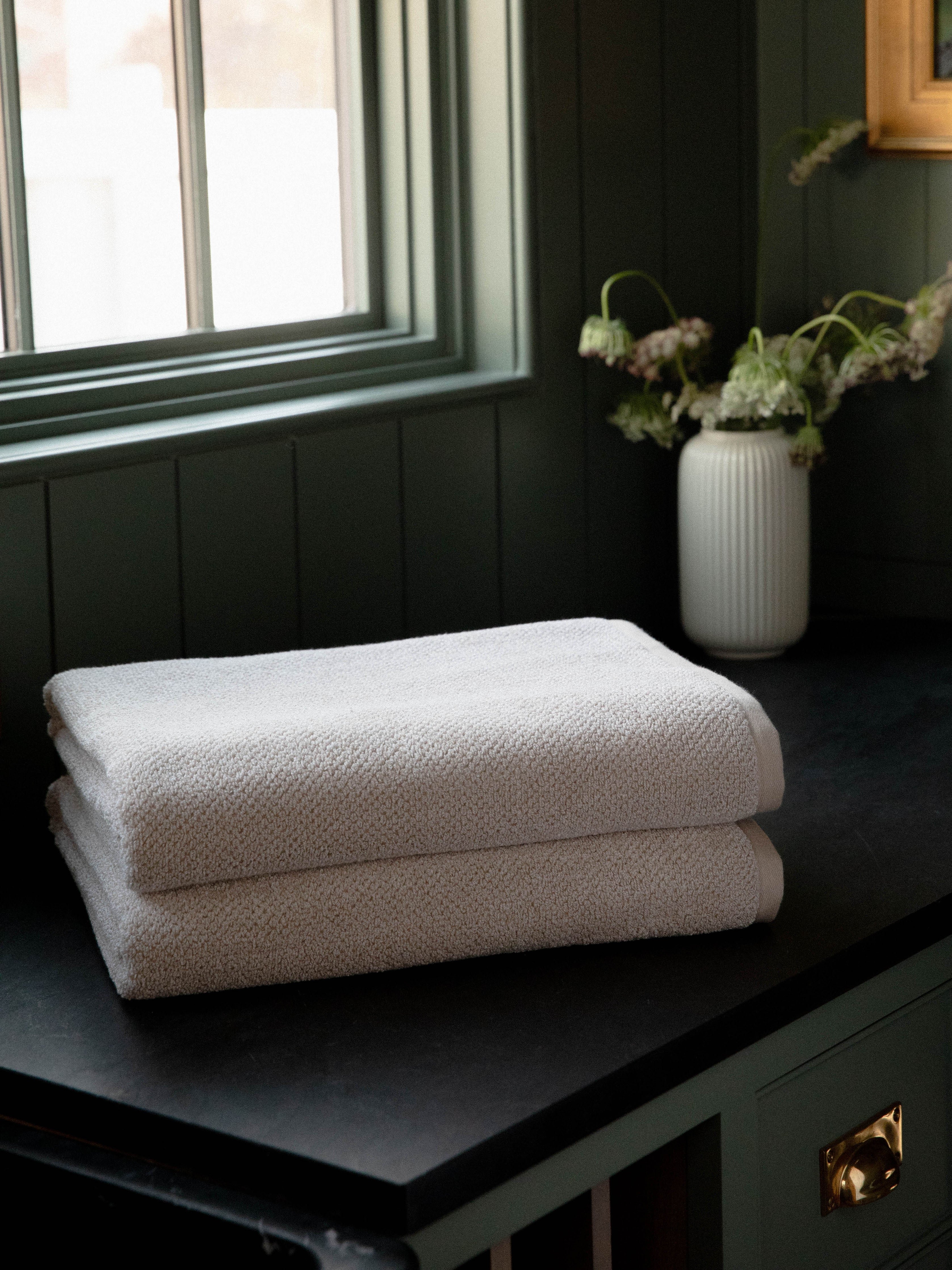 Nantucket Bath Sheets in the color Heathered Sand. Photo of Nantucket Bath Sheets taken with the bath Sheets resting on a countertop in a bathroom. 