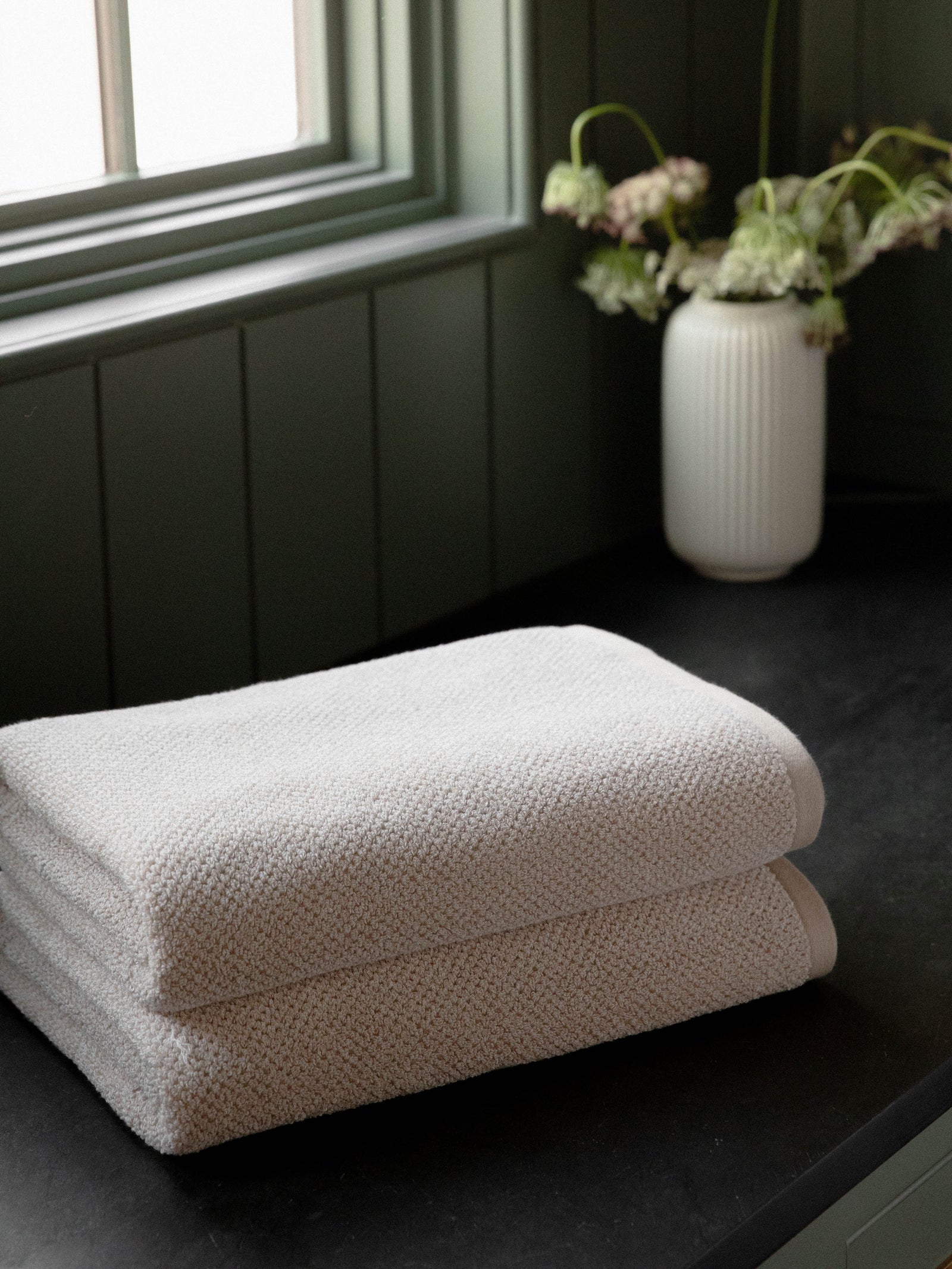 Nantucket Bath Towels in the color Heathered Sand. Photo of Nantucket Bath Towels taken with the bath towels resting on a countertop in a bathroom. 