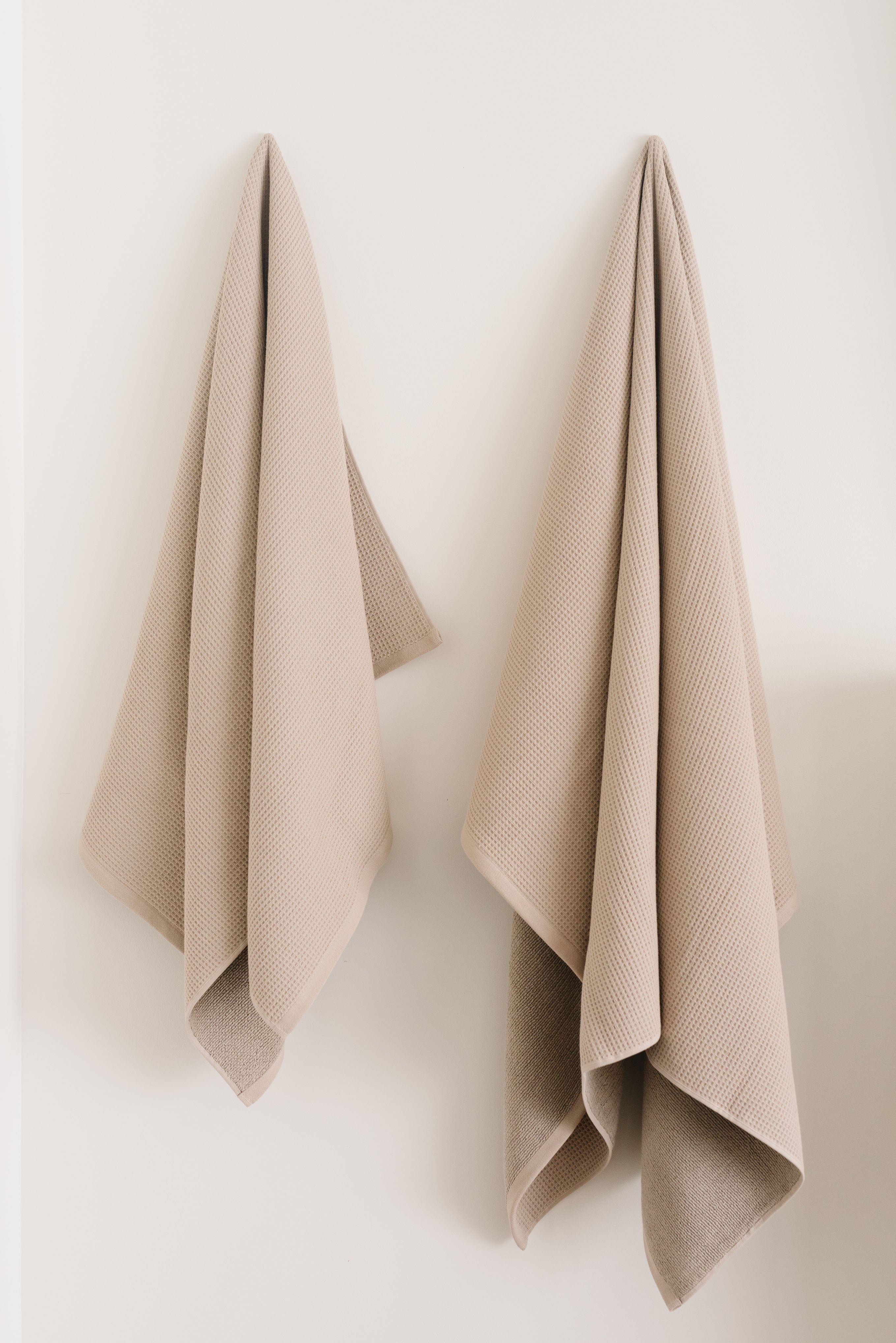 Waffle Bath Towel in the color Sand. Photo of Sand Waffle Bath Towel taken hanging from a towel hook in a white bathroom. The towel hook is not seen. 
