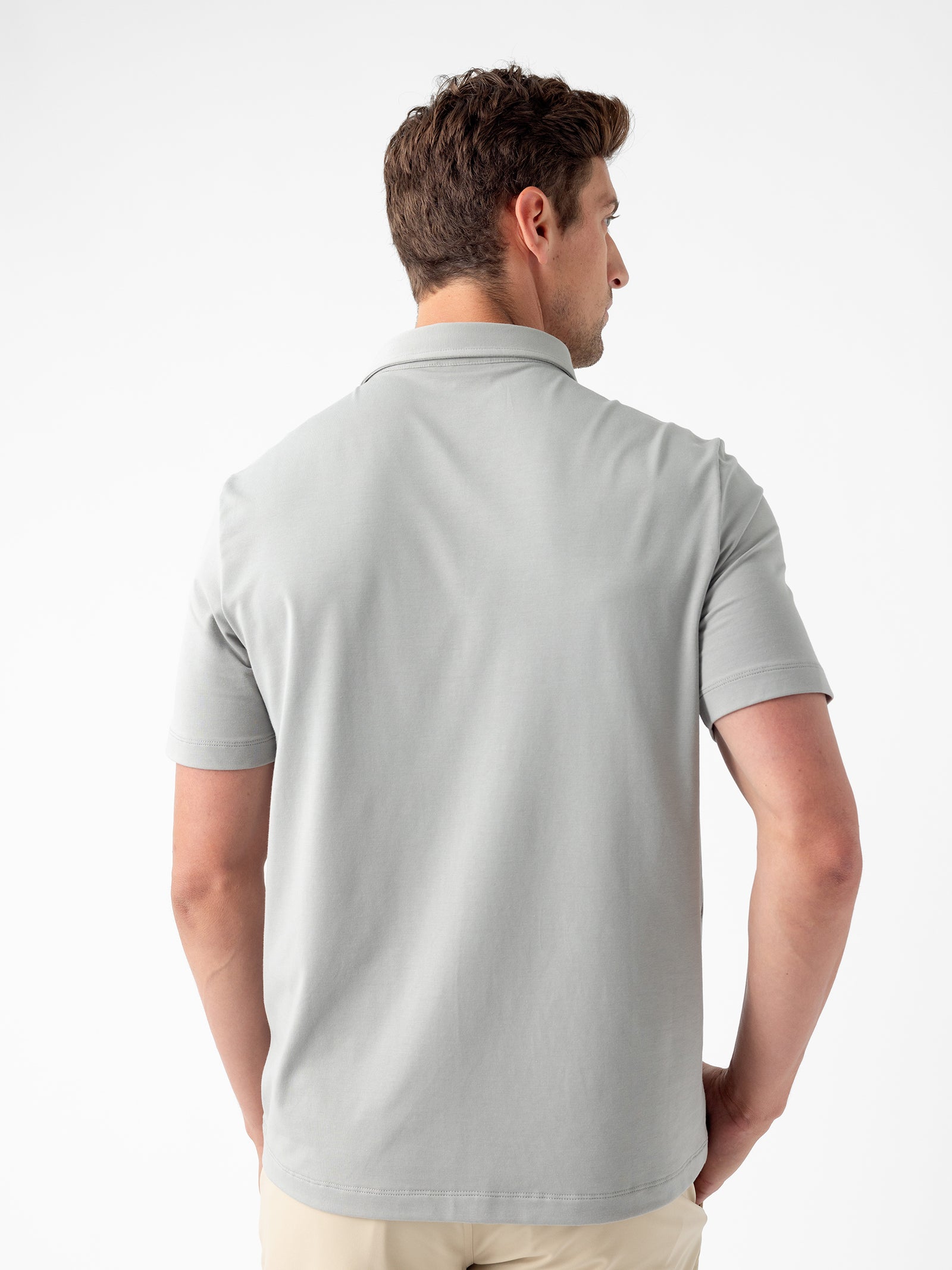 A man with short brown hair, seen from behind, is wearing the Cozy Earth Men's Everyday Polo in light gray. He has his hands on his hips and is standing against a white background. 