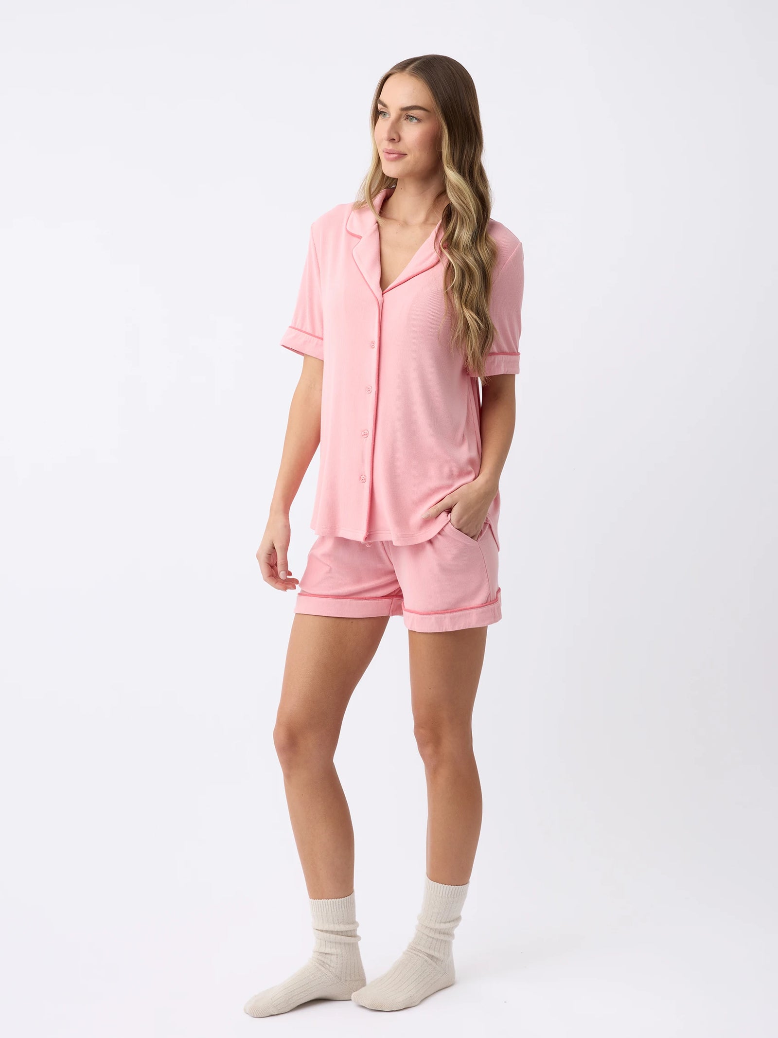 A person with long hair wears the Women's Bamboo Rib-Knit Classic Short Sleeve Pajama Top by Cozy Earth, paired with matching shorts and light-colored socks, standing against a plain background. 