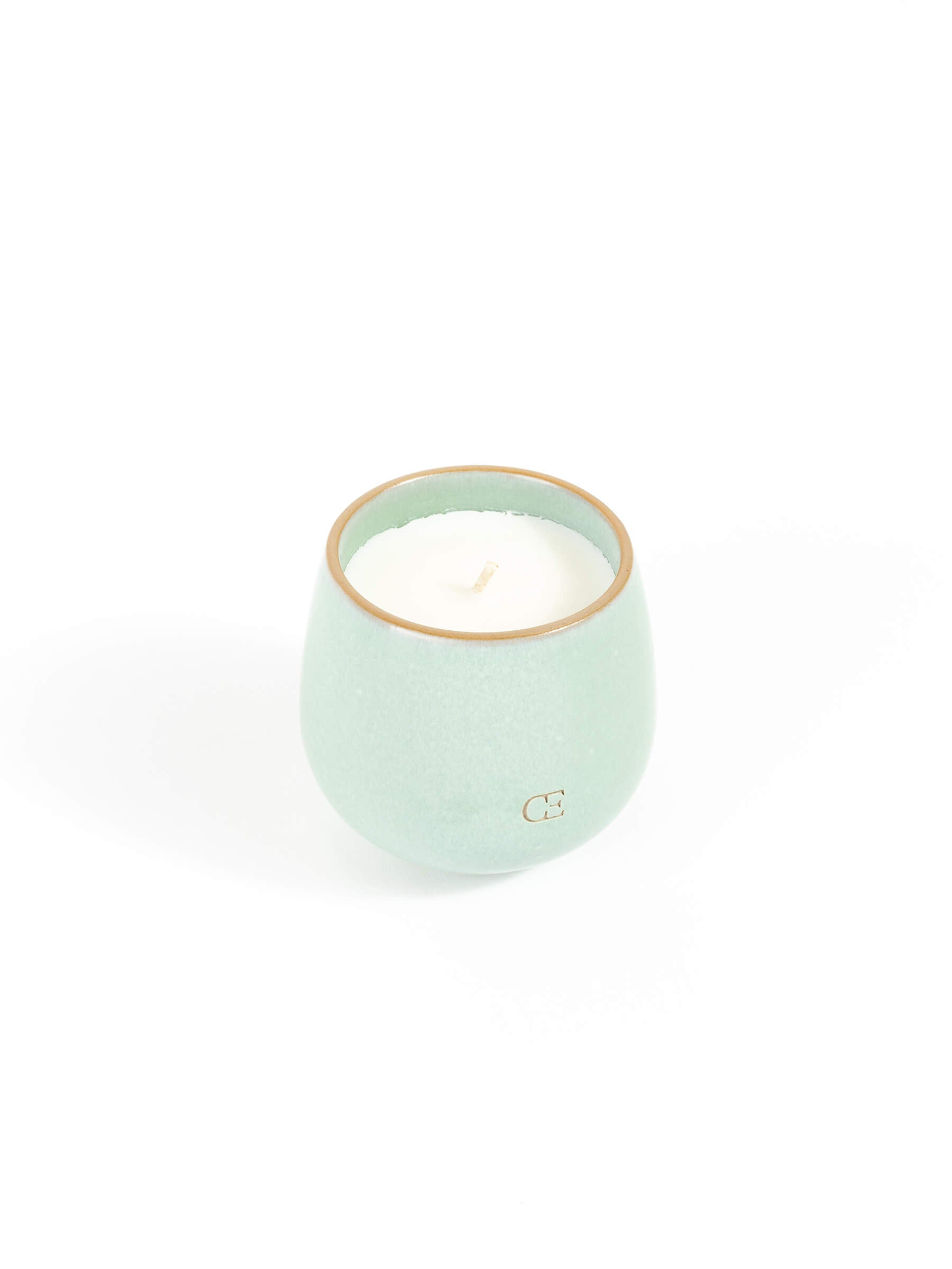 The Cozy Earth Candle UNWIND is a small, round, light green ceramic holder with a white candle inside, shown against a plain white background.