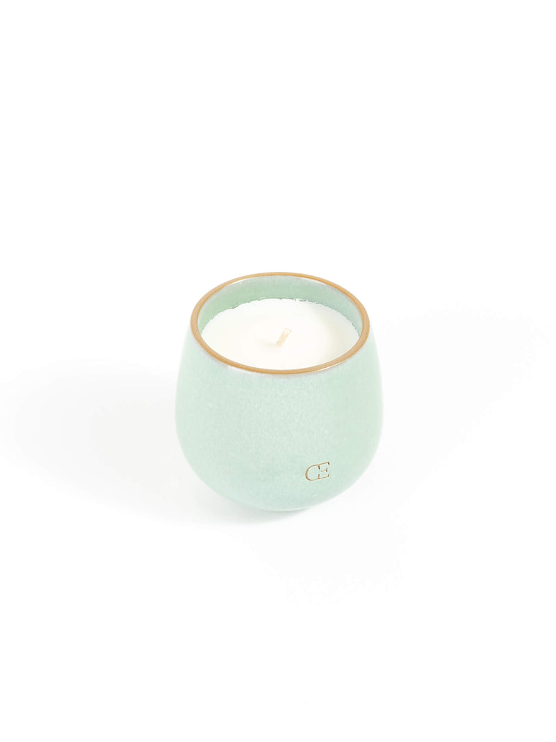 The Cozy Earth Candle UNWIND is a small, round, light green ceramic holder with a white candle inside, shown against a plain white background.