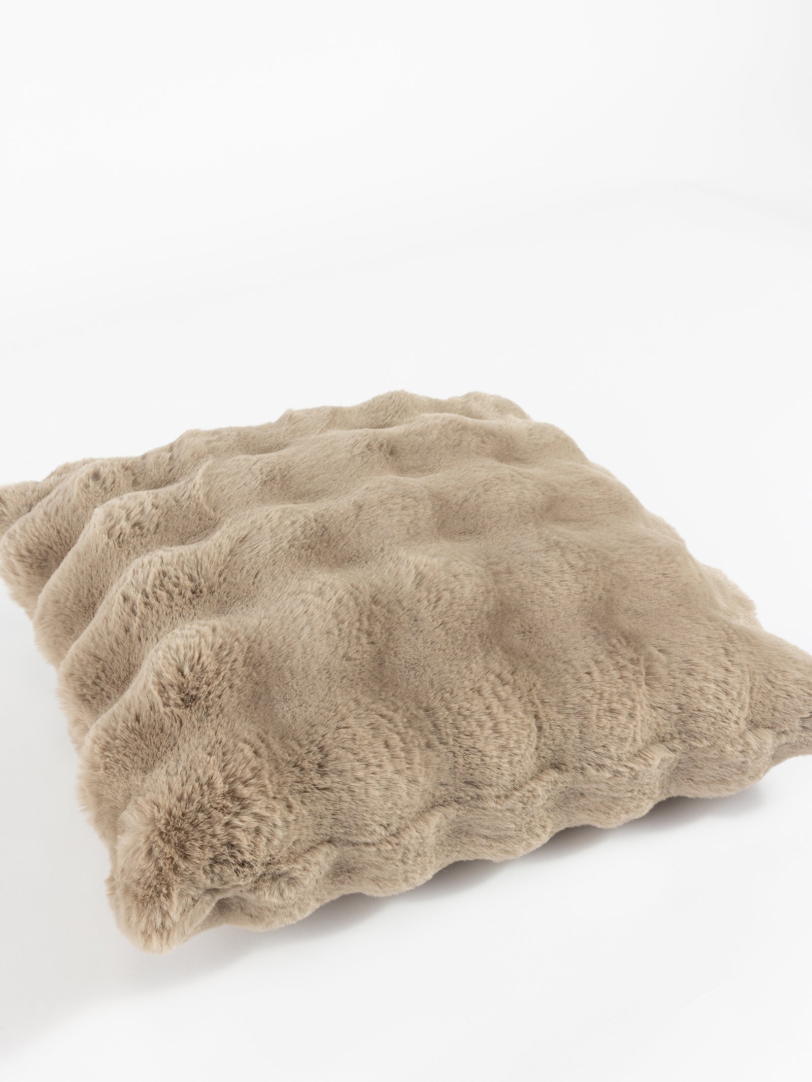 A Bubble Cuddle Pillow from Cozy Earth, featuring a fluffy beige design with a wavy texture, is placed on a white surface. Its soft, plush appearance adds a touch of coziness. 