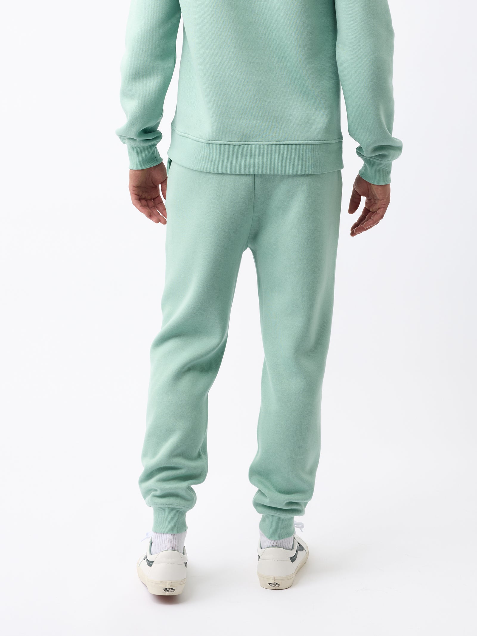 Rear view of a person wearing the Men's CityScape Jogger in light green from Cozy Earth and white sneakers against a white background. 