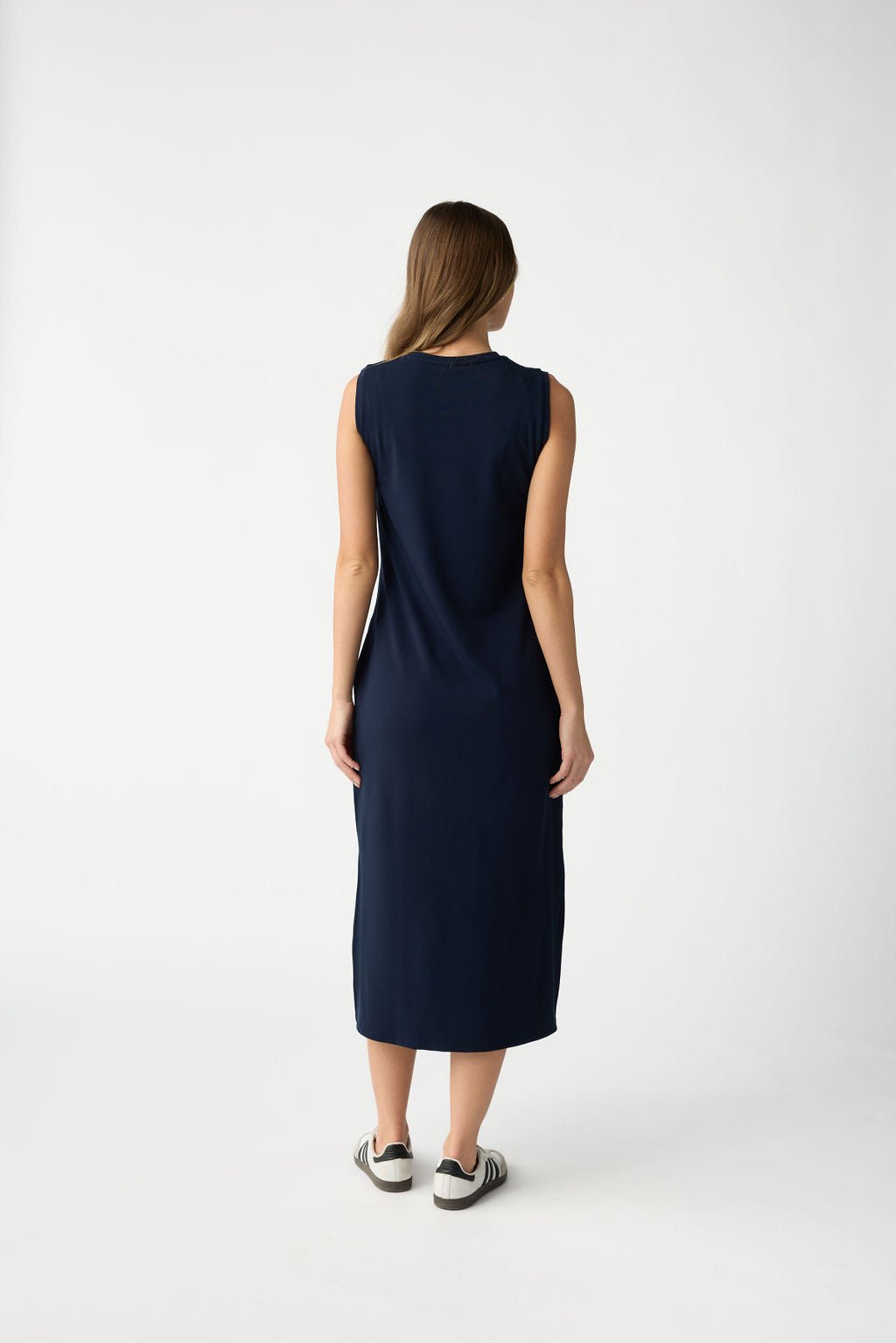 A woman with long brown hair is facing away from the camera on a plain white background, wearing a Cozy Earth Women's Brushed Bamboo Sleeveless Midi Dress and black and white sneakers. |Color:Navy