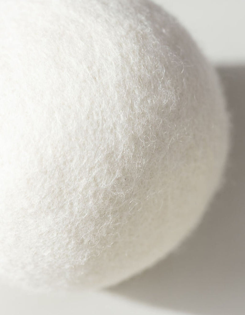 Close-up of a white, textured Wool Dryer Ball by Cozy Earth, made of felted wool, with soft lighting and a gentle shadow on a light surface.