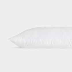 A white **Silk Pillow** from **Cozy Earth** lies horizontally against a plain white background, showcasing a clean and smooth surface with faint stitching along the edge, giving it a fresh and fluffy appearance.