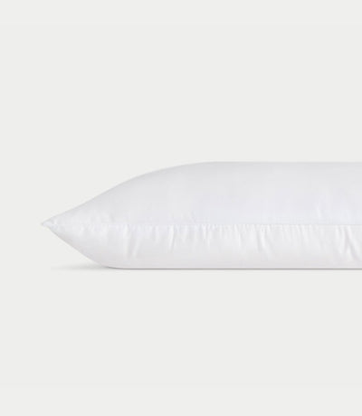 A white **Silk Pillow** from **Cozy Earth** lies horizontally against a plain white background, showcasing a clean and smooth surface with faint stitching along the edge, giving it a fresh and fluffy appearance.