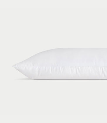 A white **Silk Pillow** from **Cozy Earth** lies horizontally against a plain white background, showcasing a clean and smooth surface with faint stitching along the edge, giving it a fresh and fluffy appearance.