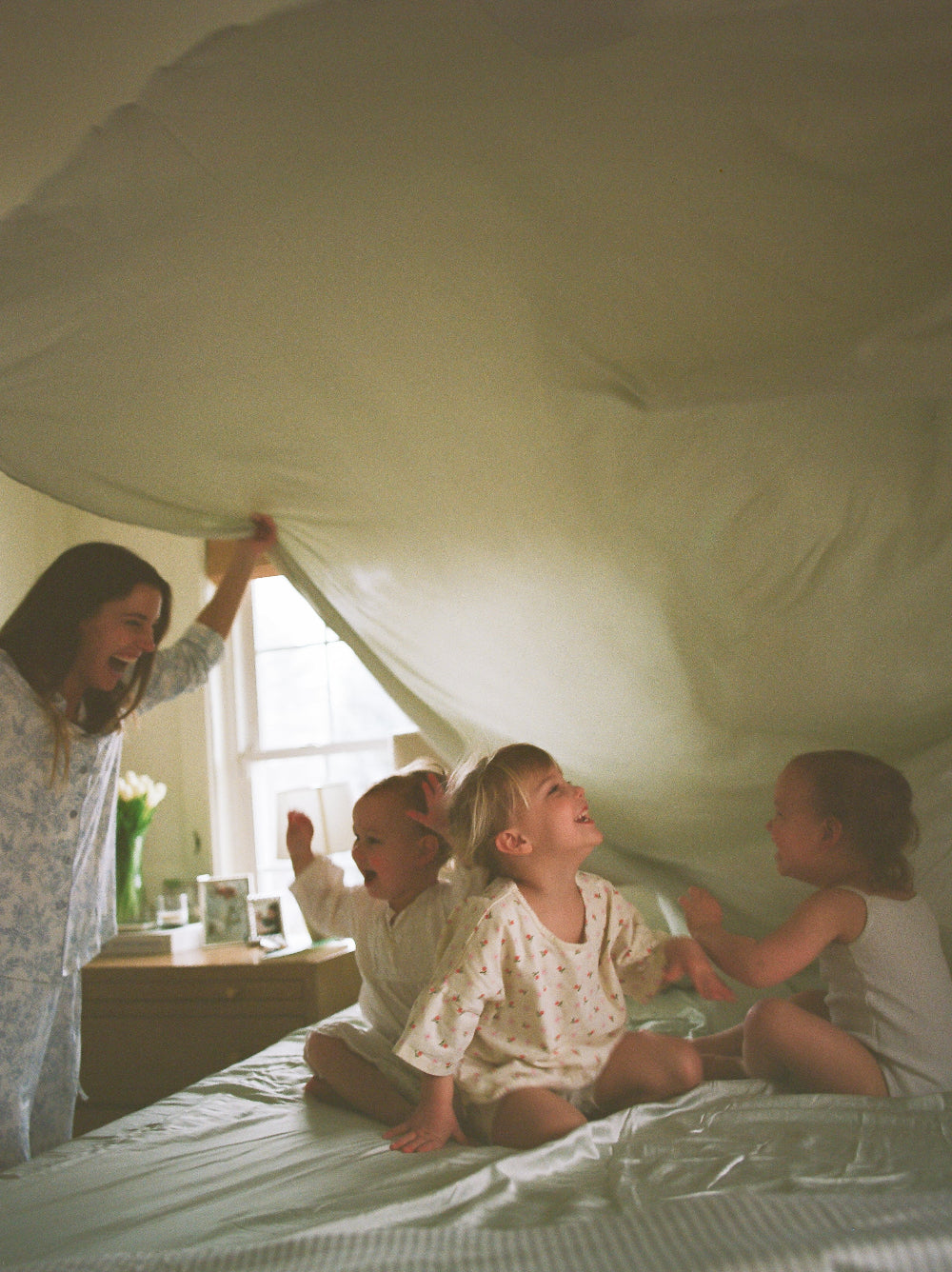 Woman and children playing under a white sheet on a bed