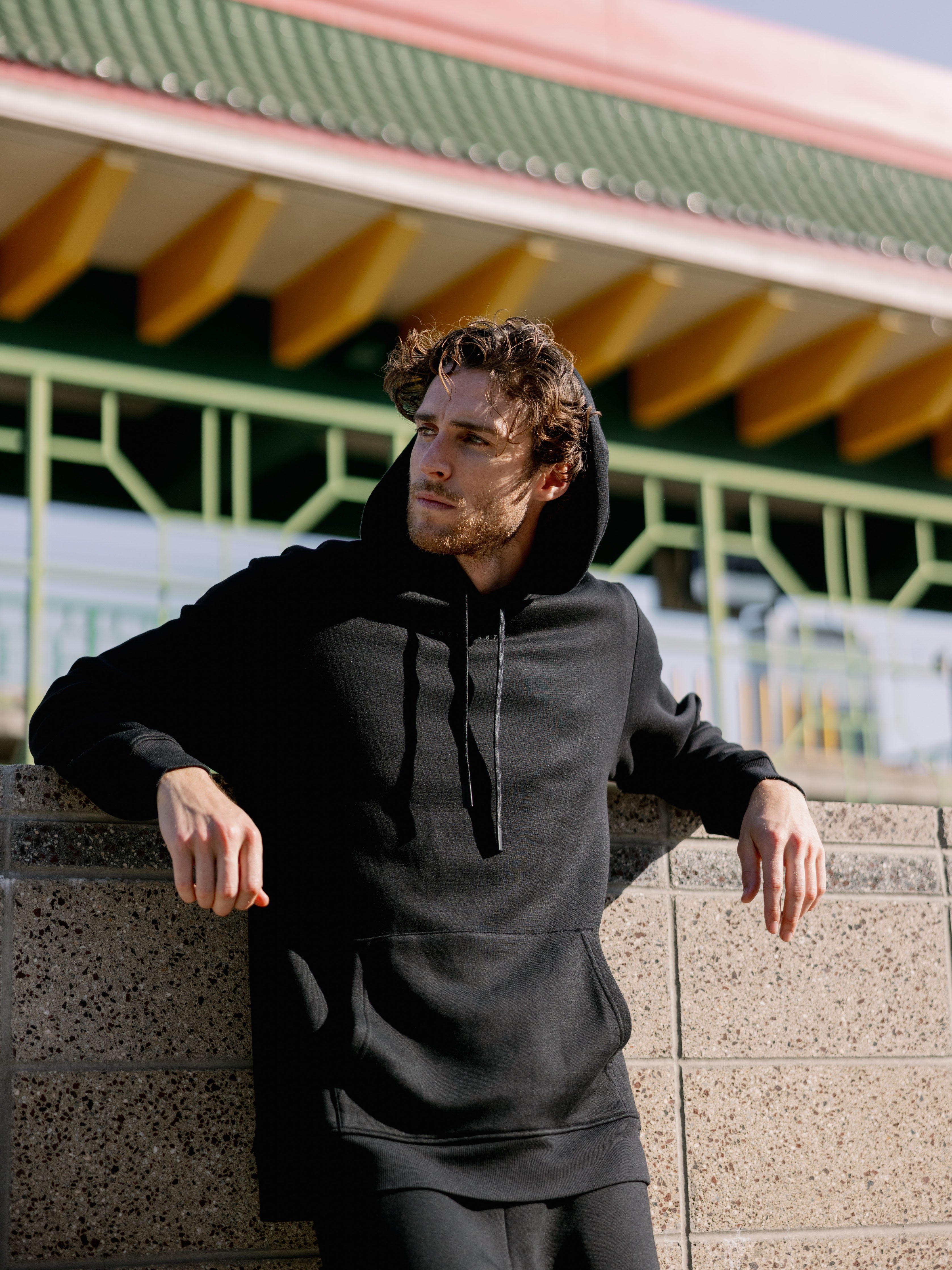 Man in black cityscape hoodie leaning against wall 