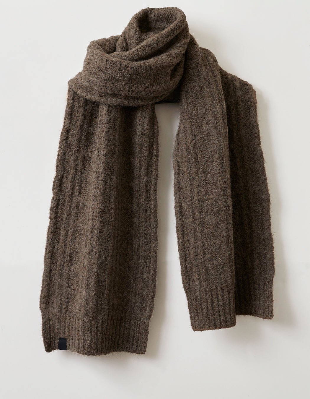 The Cozy Earth Cable Knit Scarf, featuring a thick brown textured pattern, is displayed hanging loosely against a plain white background.
