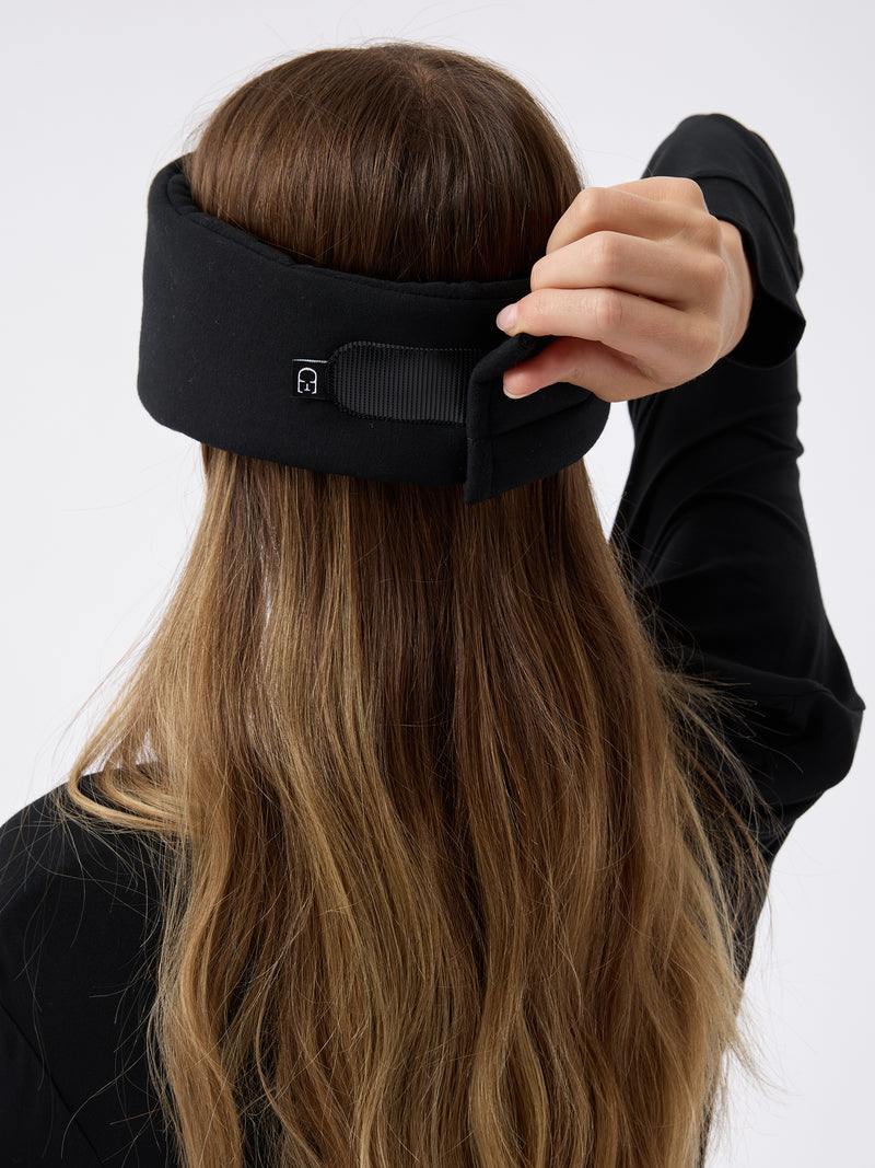 A woman wears the Cozy Earth Adjustable Bamboo Sleep Mask in Black. She is facing away and showing where the mask fastens at the back.