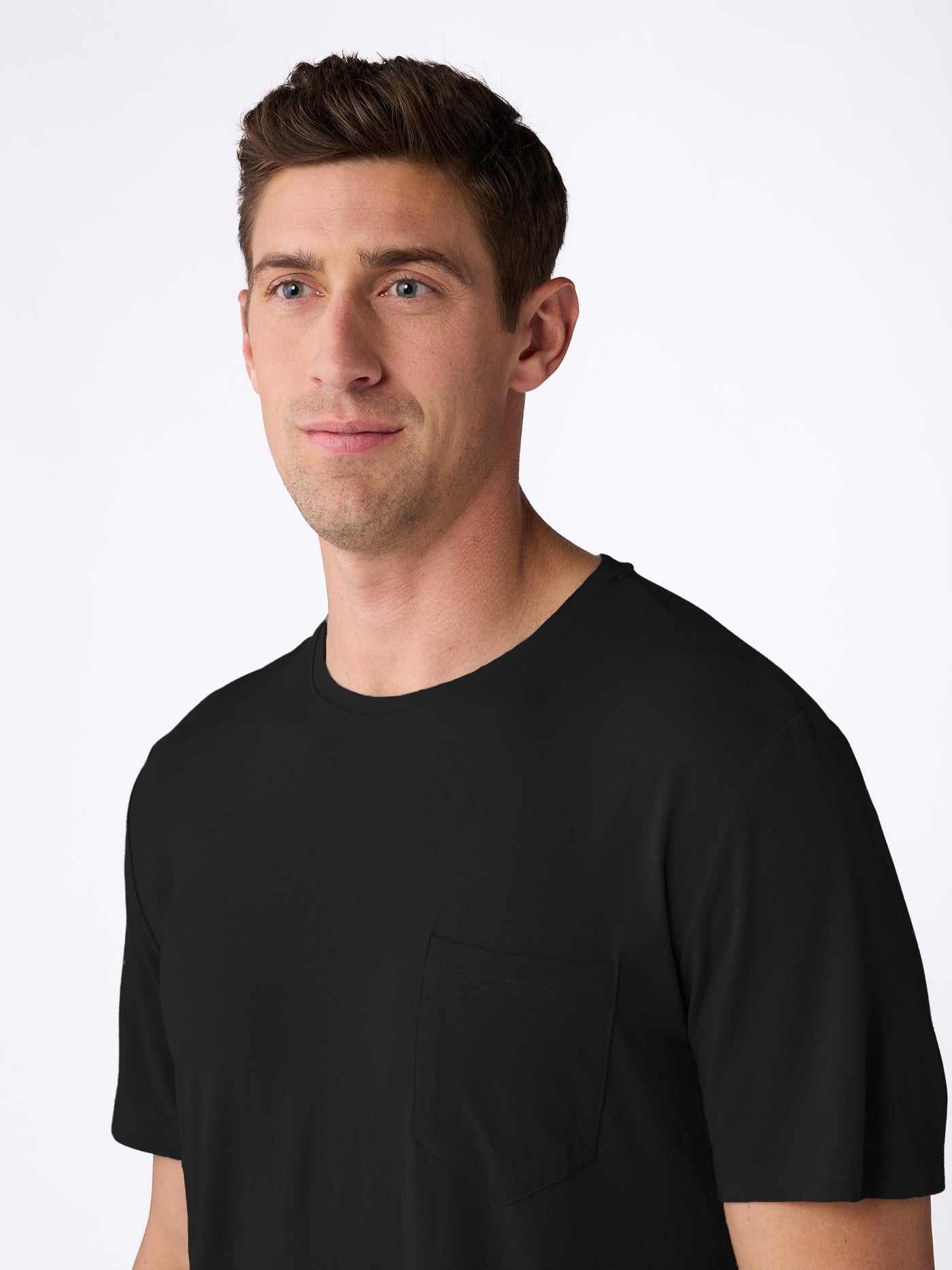 A man with short brown hair wears the Cozy Earth Men's Bamboo Stretch-Knit Short Sleeve Pajama Set, featuring a black crew neck top with a front pocket, standing against a plain white background and looking slightly to the side.