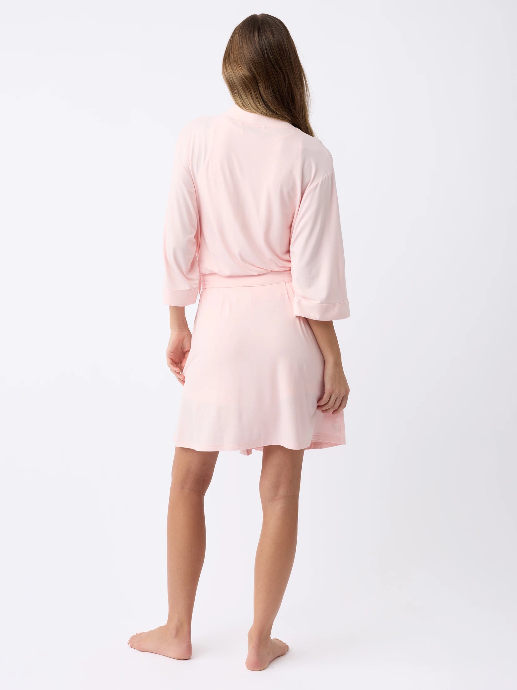 A barefoot individual is shown from behind wearing the Cozy Earth Women's Stretch-Knit Bamboo Kimono Robe in light pink, featuring three-quarter sleeves and a sash belt, set against a plain white background. |Color:Blossom