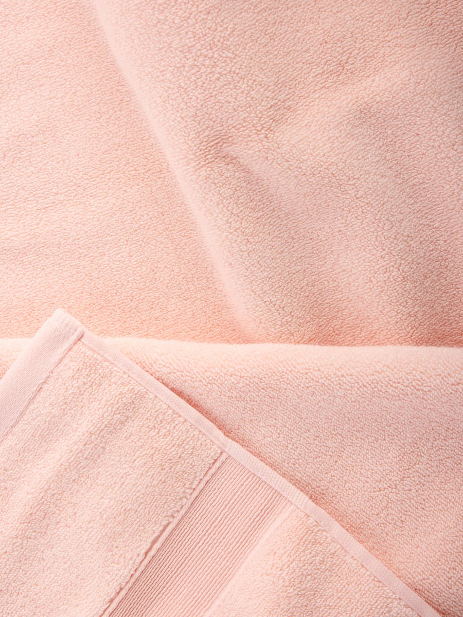 A close-up of the Complete Luxe Bath Bundle from Cozy Earth reveals a plush, peach-colored towel with a textured surface. The neatly folded edges exude warmth and coziness, enhancing the sense of comfort. 