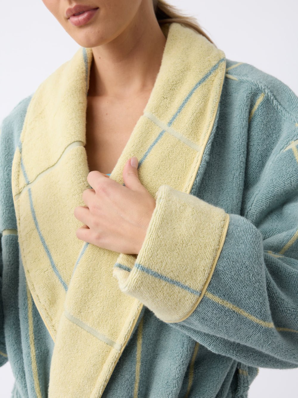 A person wearing the Cozy Earth Windowpane Resort Robe with yellow cuffs and collar holds the collar in one hand. The robe showcases a blue and yellow plaid pattern against a plain white background. |Color:Blue Lagoon