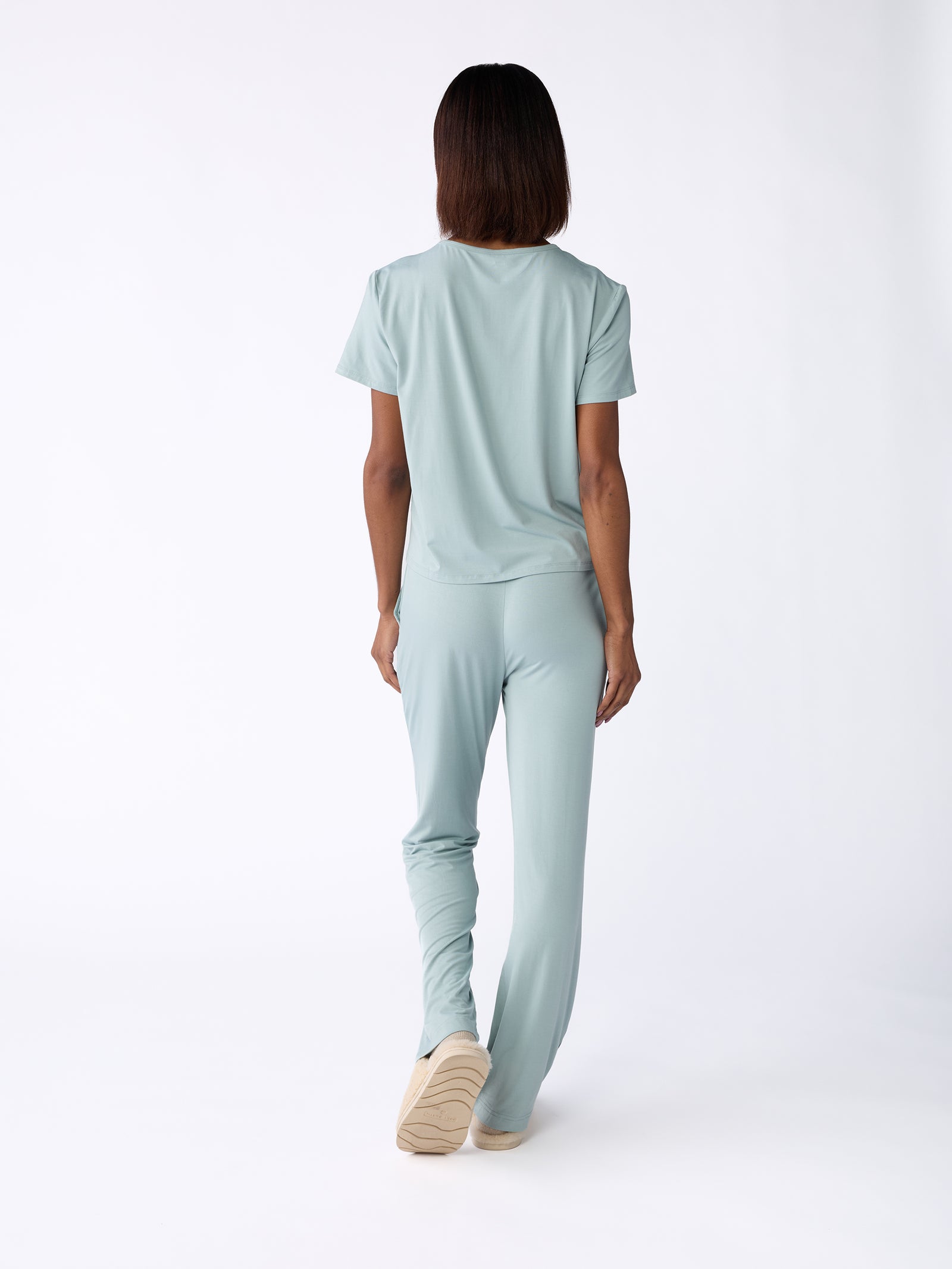 A person with short hair is seen from behind, dressed in the light blue Women's Stretch-Knit Bamboo Lounge Tee by Cozy Earth, paired with matching pants. They are set against a plain white background. 