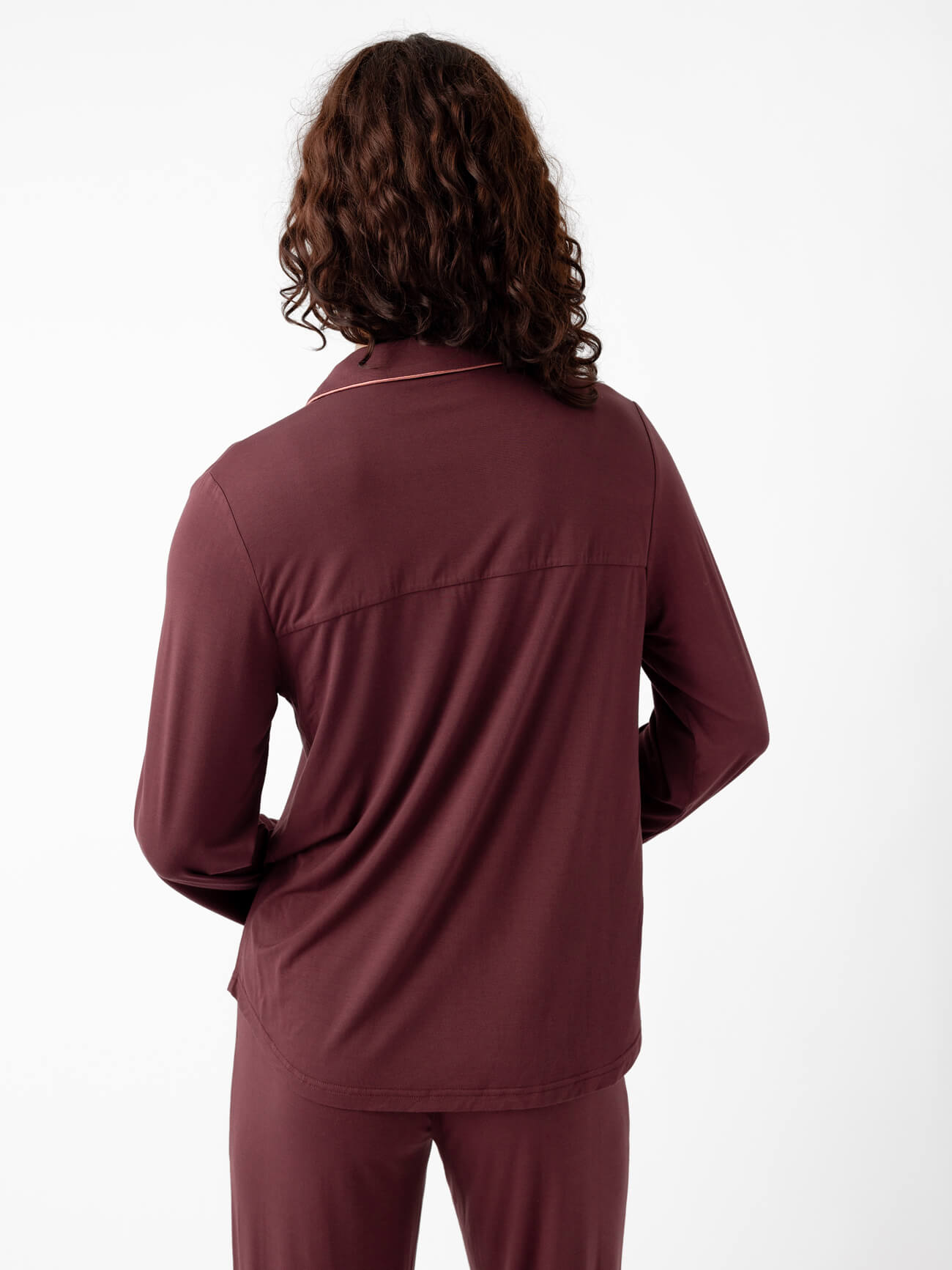Rear view of a person with long curly hair wearing the Last Chance Women's Bamboo Stretch-Knit Pajama Set by Cozy Earth, featuring a maroon long-sleeve top and pants, against a plain white background. 