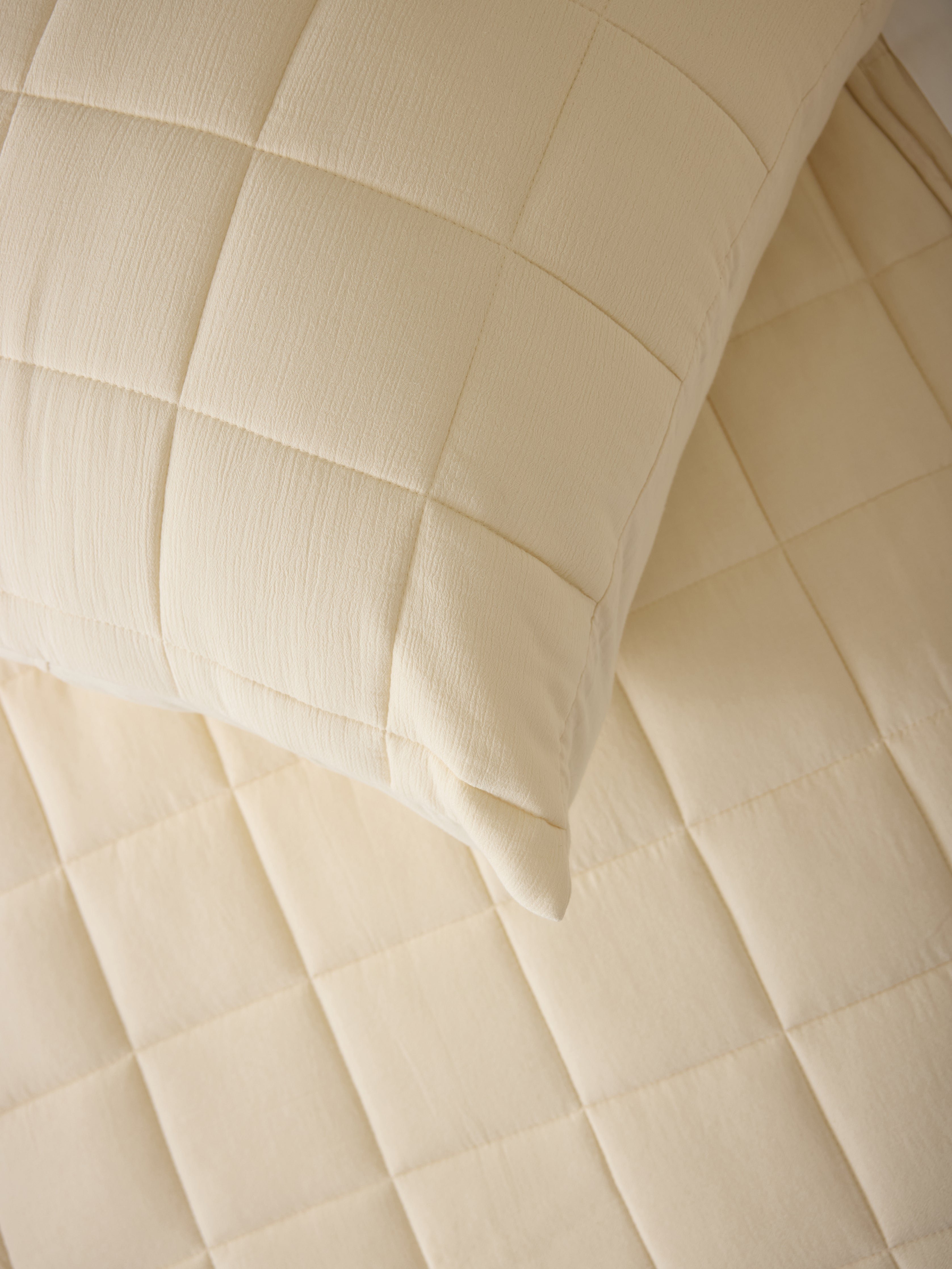 Close up of Buttermilk Aire Bamboo Box Quilt Euro Sham. The sham is resting on a bed in a bedroom|Color:Buttermilk|Size:Euro