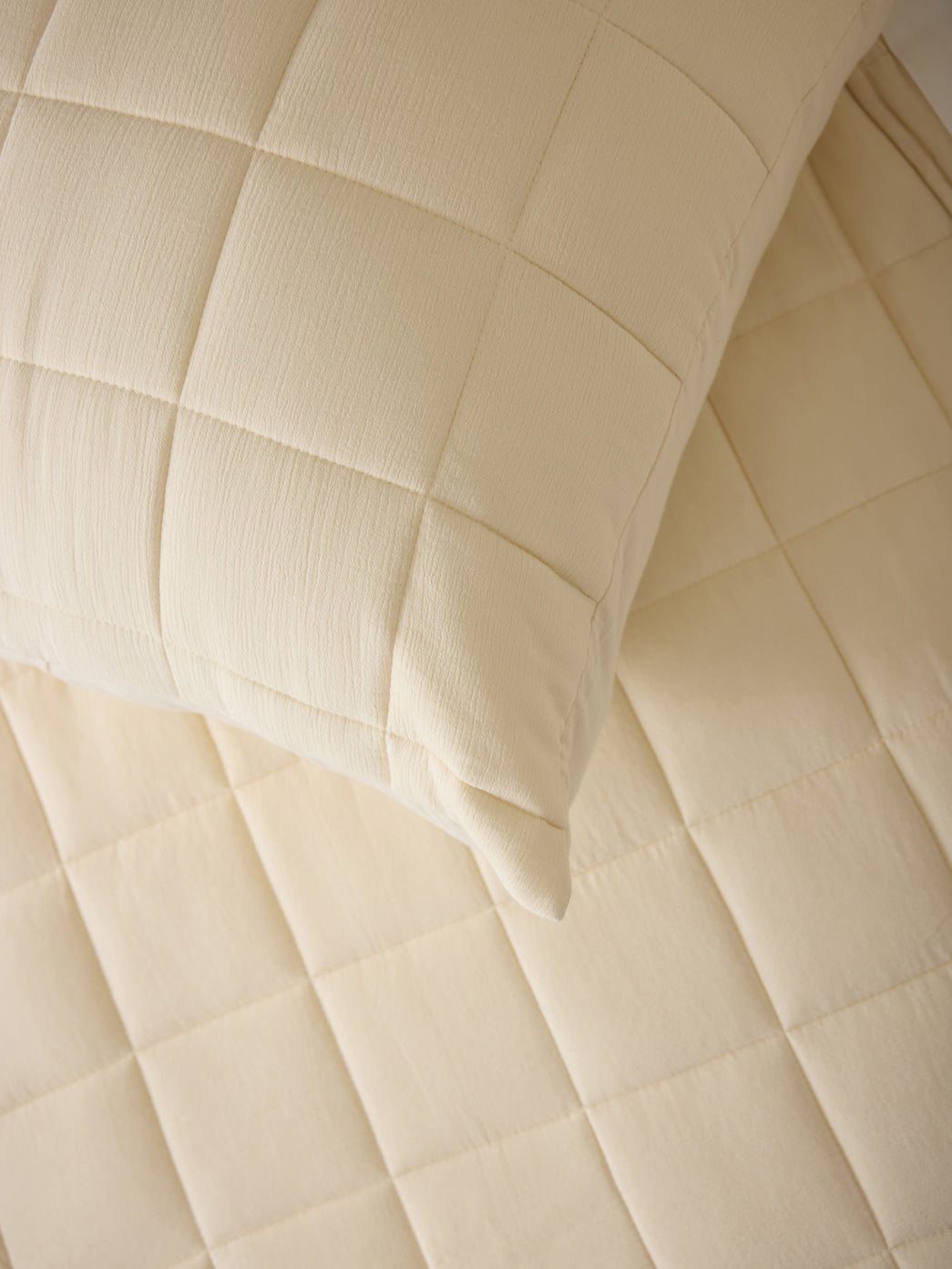 Close up of Buttermilk Aire Bamboo Box Quilt Euro Sham. The sham is resting on a bed in a bedroom|Color:Buttermilk|Size:Euro