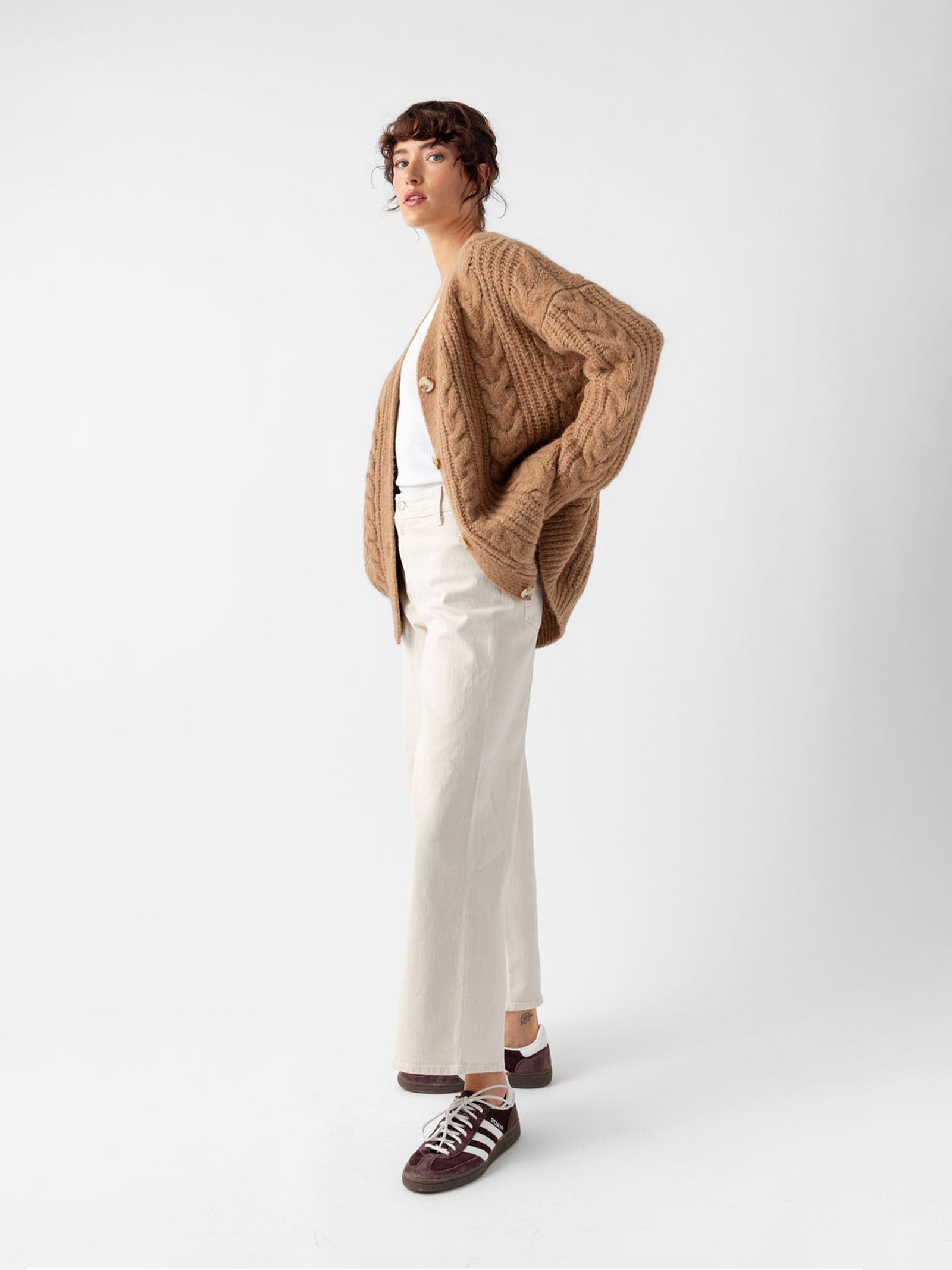 Side view of woman wearing camel cardigan and off-white pants with white background 